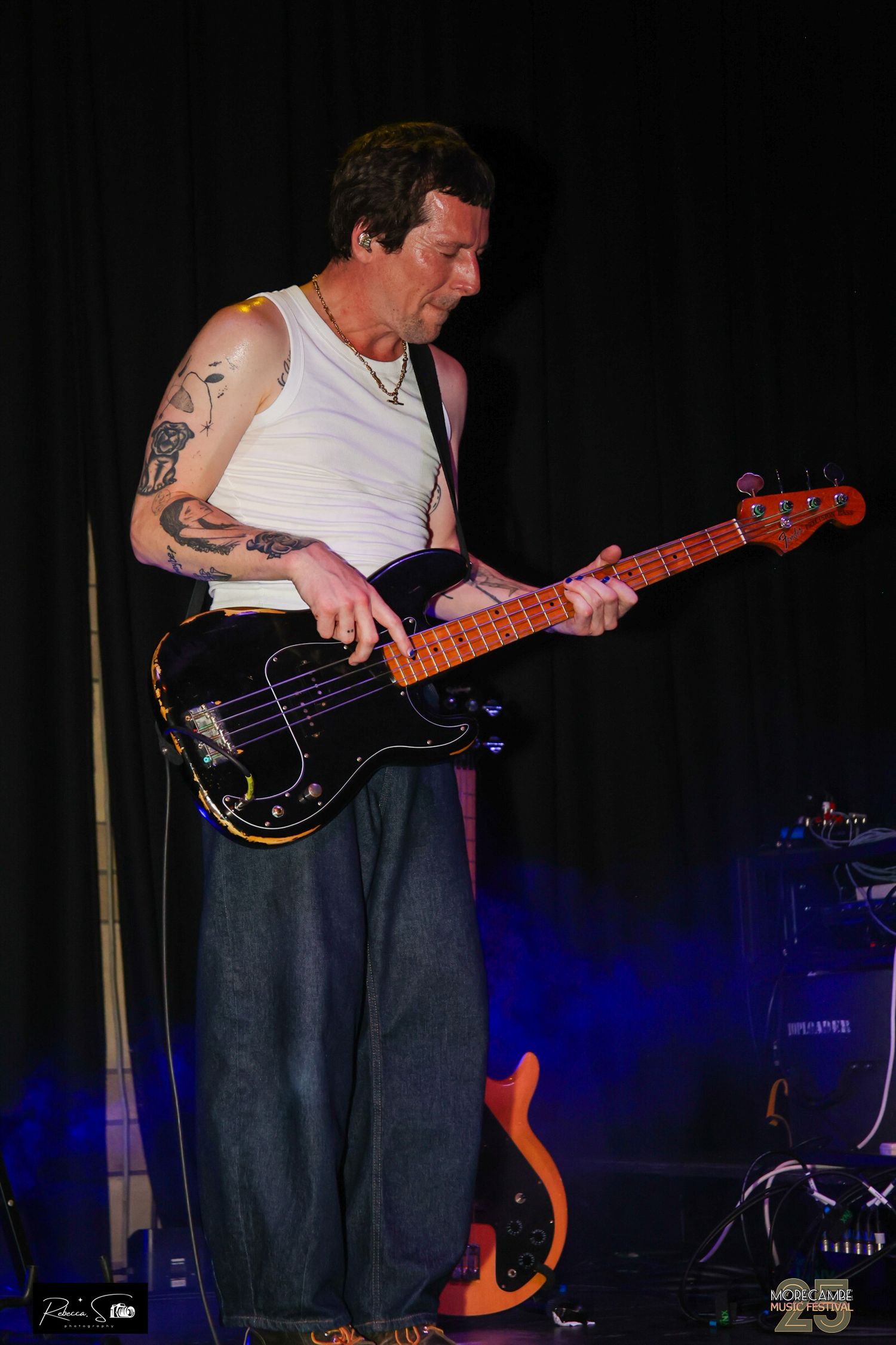 Bassist performs energetically on stage with tattoos visible in dark concert setting.