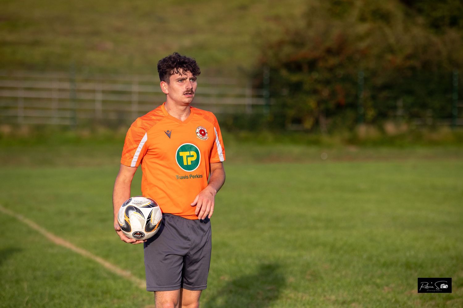 Referee in bright orange uniform stands on soccer field during a match.