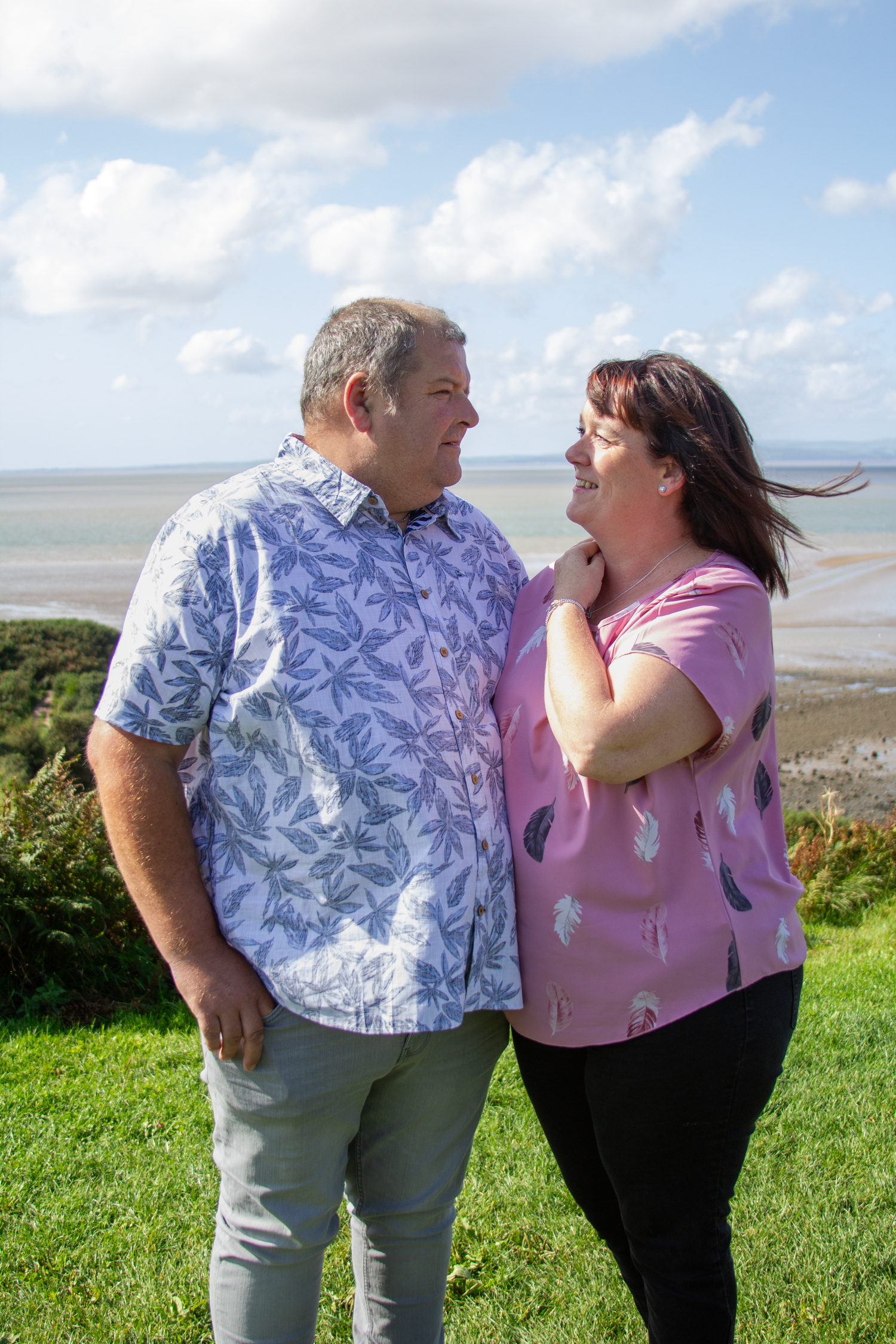 Couple enjoying a sunny day together on a grassy hillside overlooking the ocean.