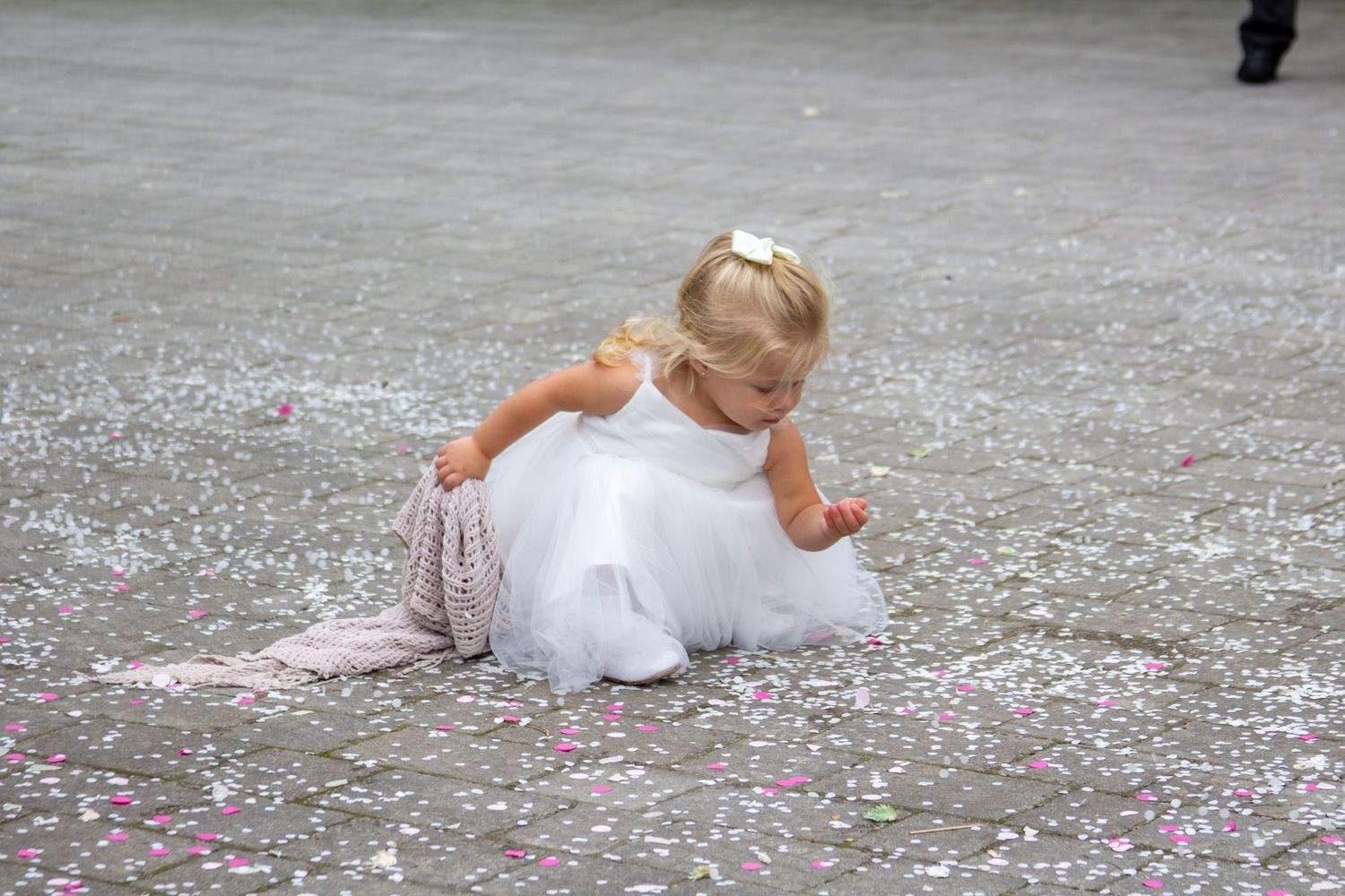 Bride in white dress playing with confetti on stone courtyard.