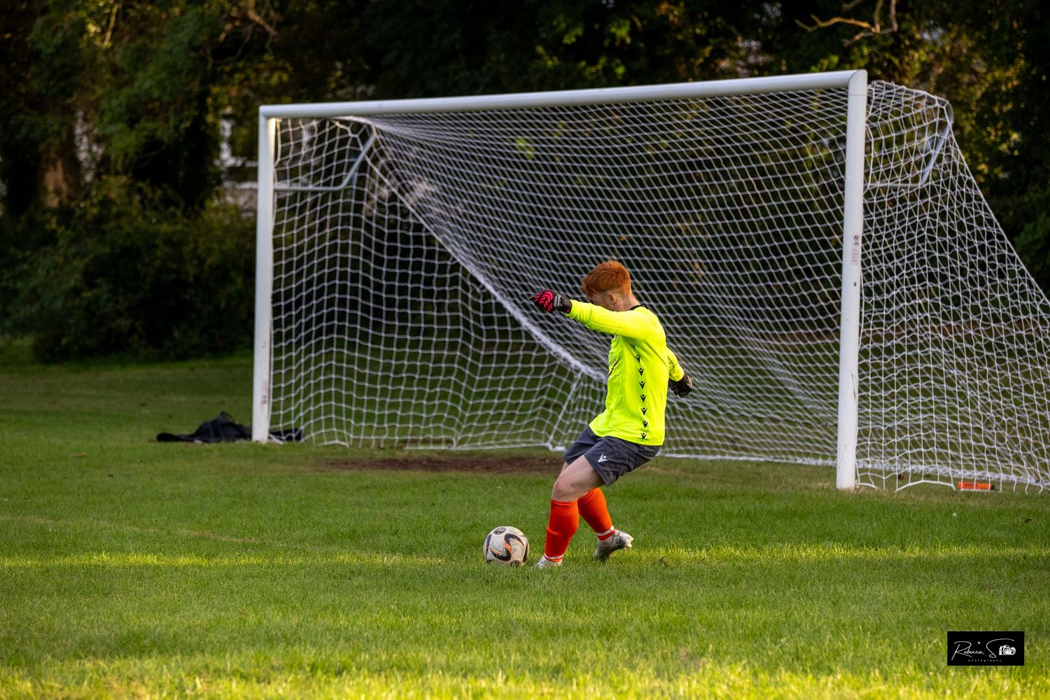 Soccer goal net stands ready on green grass field during daytime game.