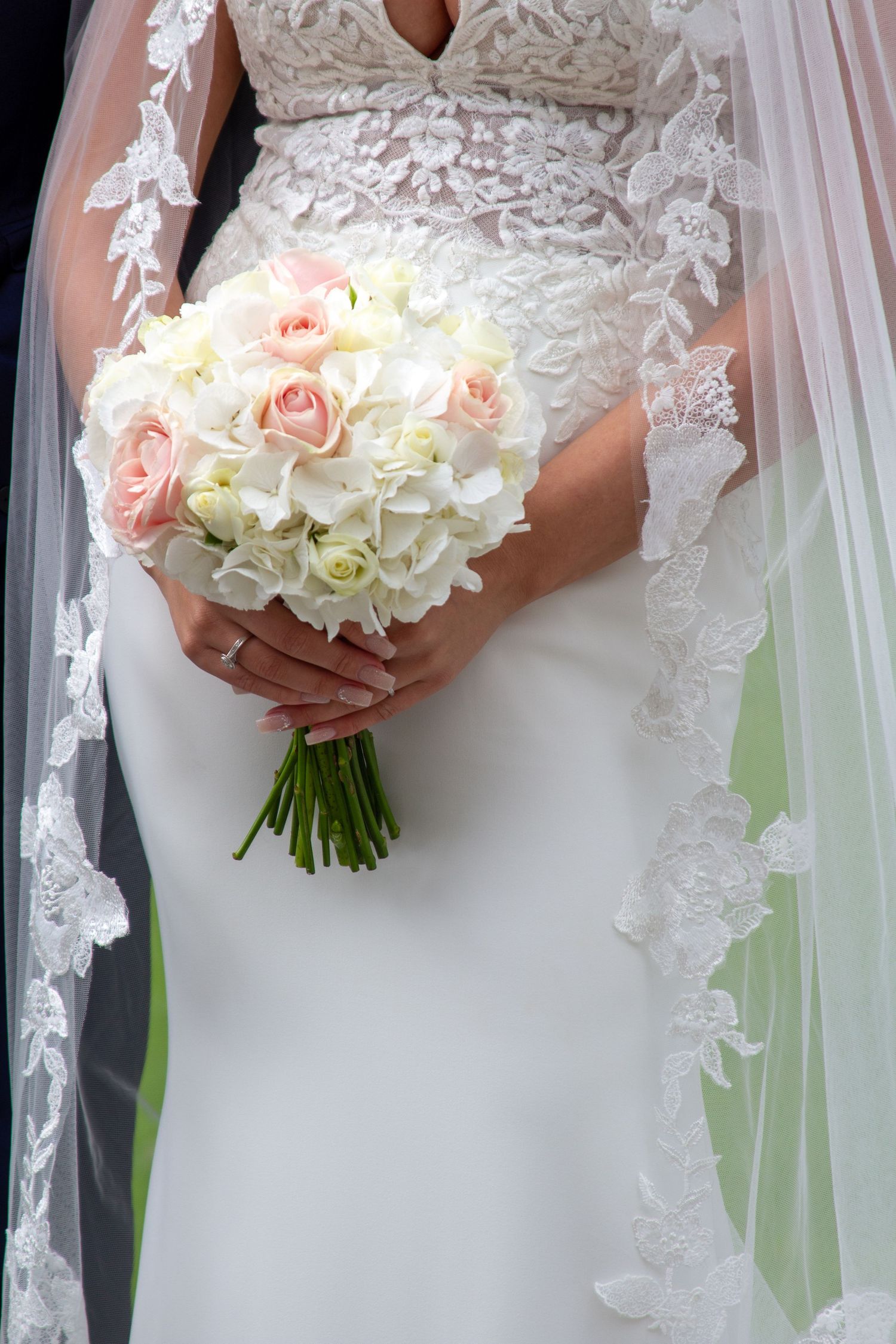 Close-up of bridal bouquet with white and blush roses against lace wedding dress.