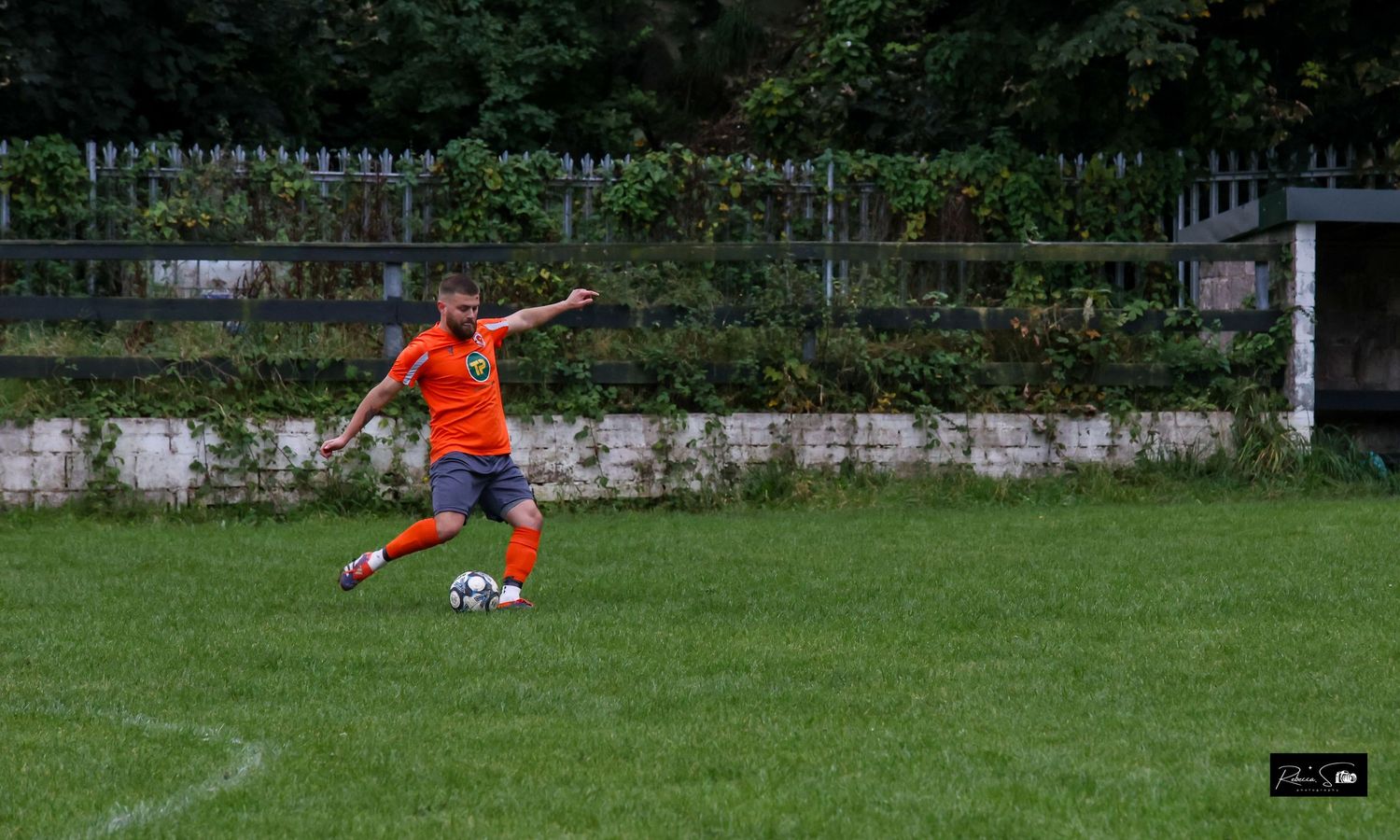 Soccer player in orange jersey kicks ball during match on grass field.