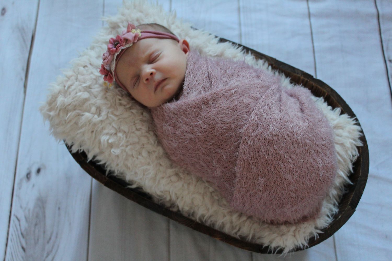 Newborn baby wrapped in pink blanket sleeping peacefully on white surface.