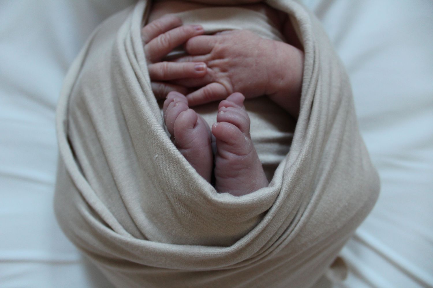 Close-up shots of newborn baby wrapped in soft white blanket.