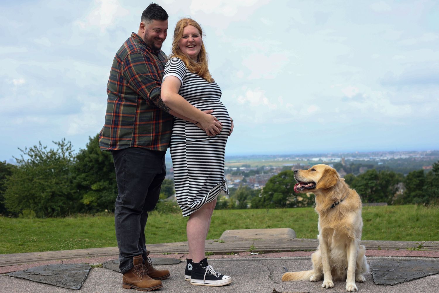 Maternity photo session with golden retriever dog overlooking city view.