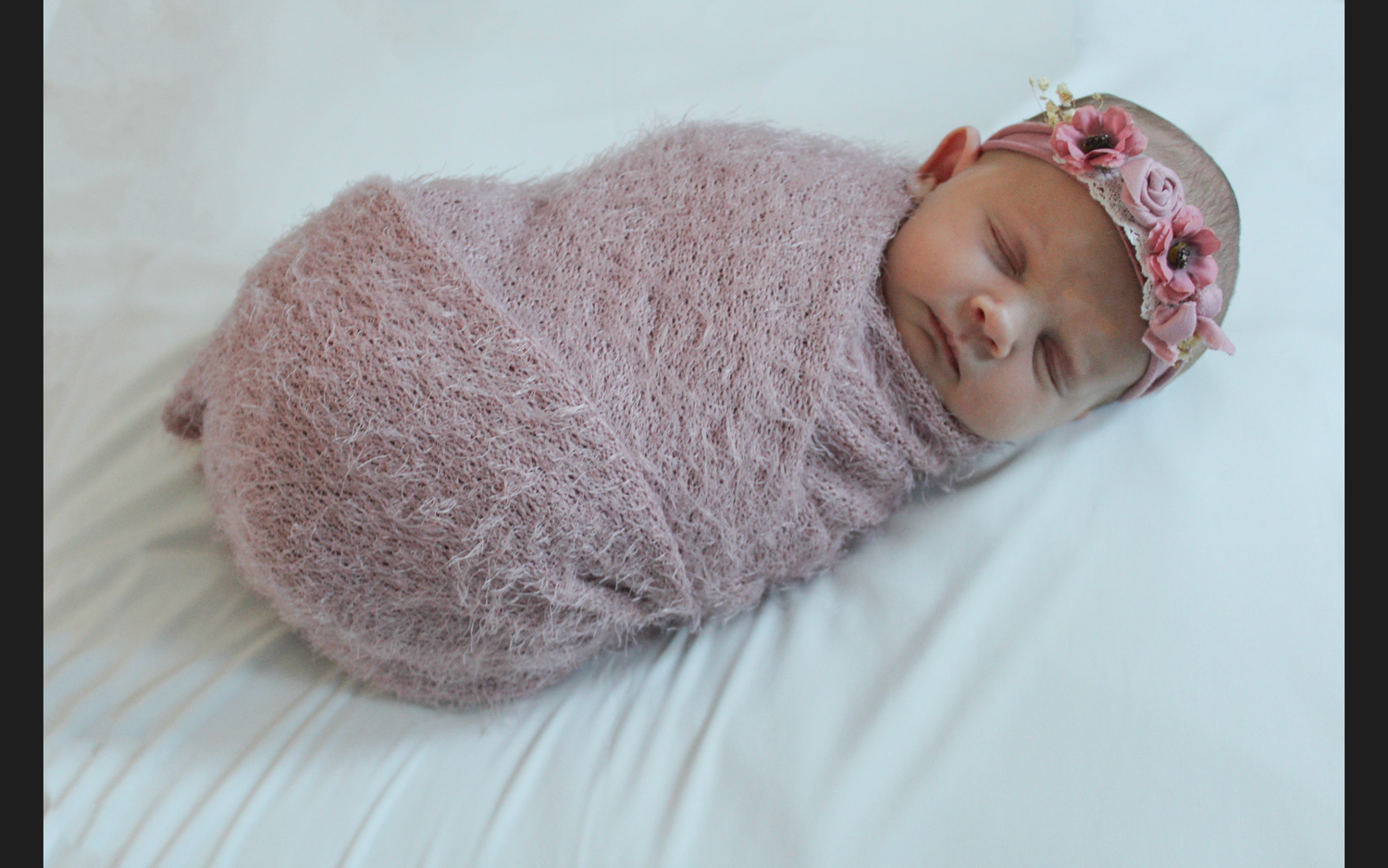 Baby wrapped in soft pink blanket lying on white surface.