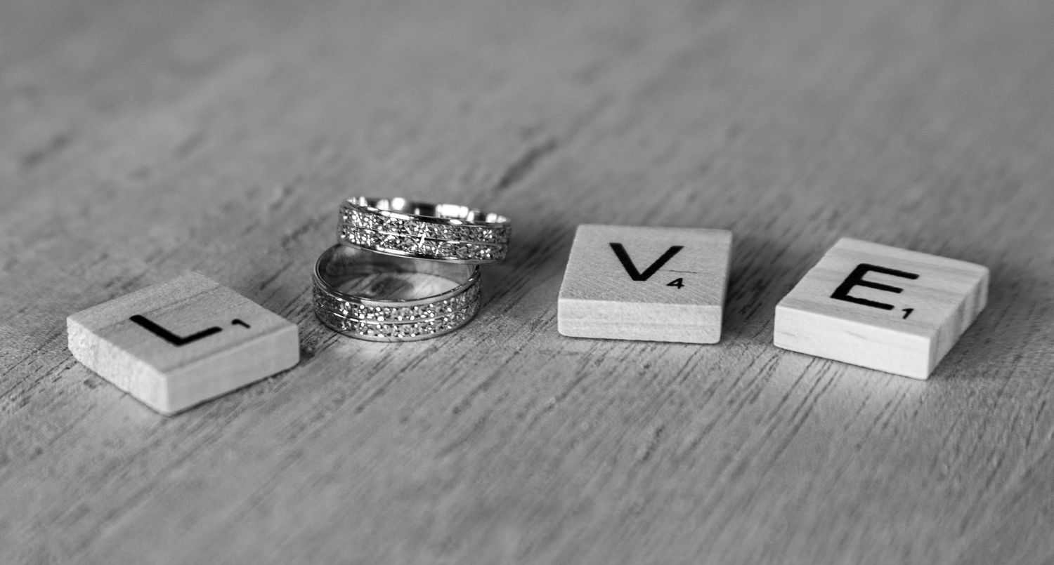 Letter blocks spelling LOVE with wedding rings on a gray wooden background.