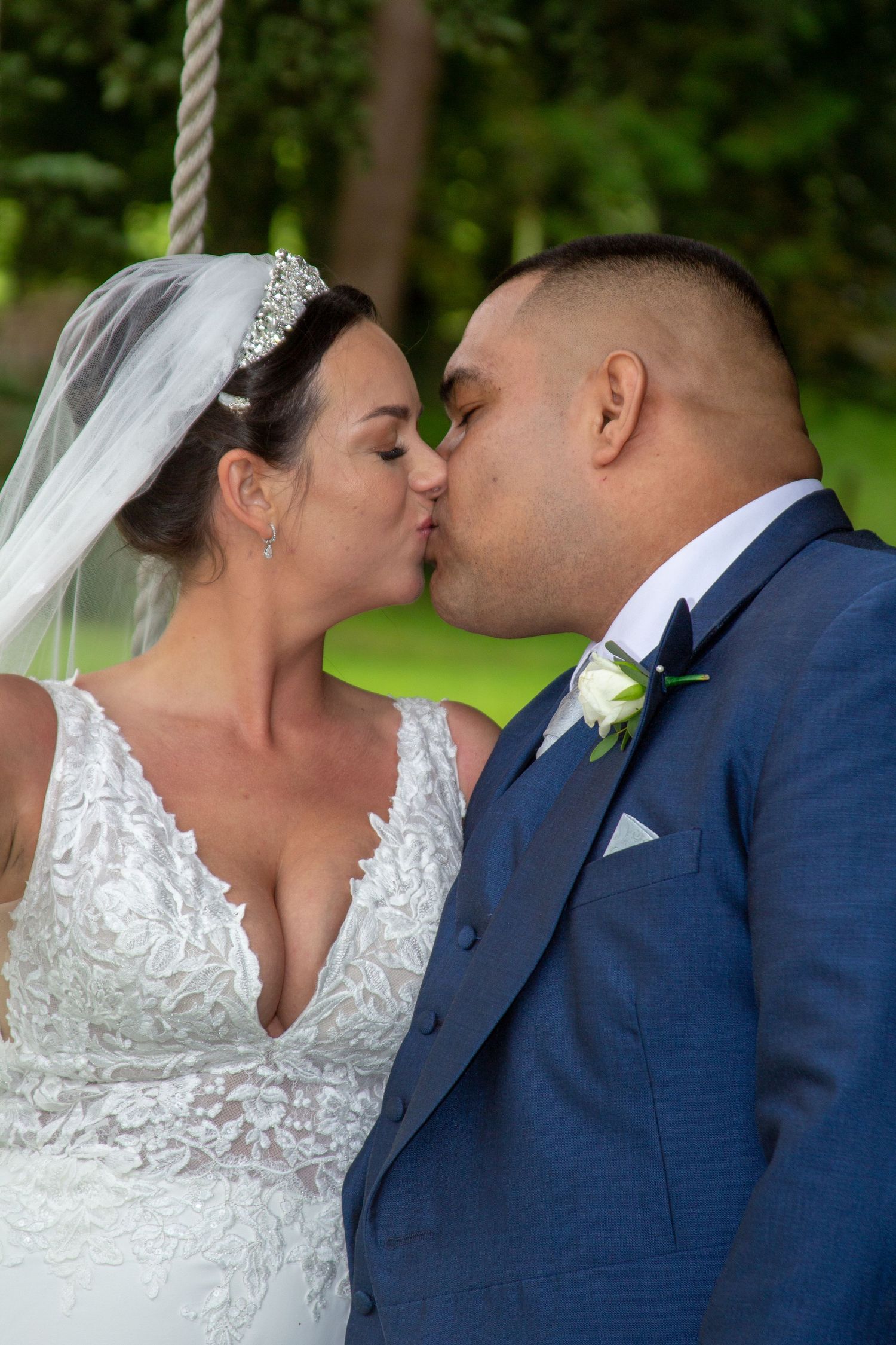 Romantic wedding moment captured in garden setting with lace dress and navy suit.