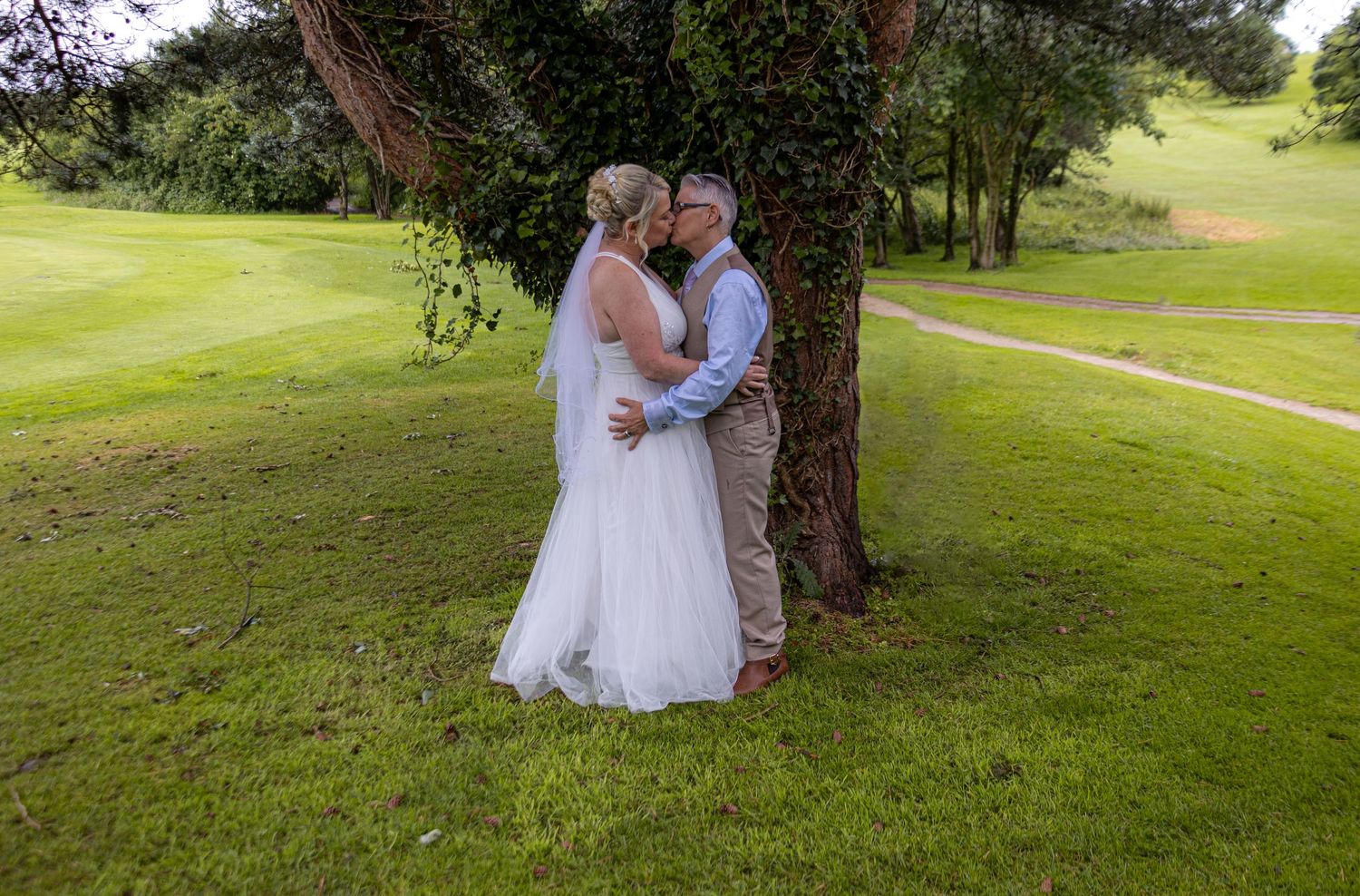 Wedding couple photos taken outdoors on a grassy hillside with trees.