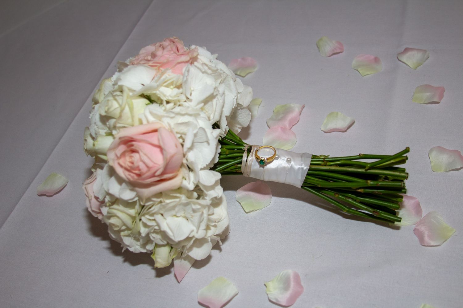 Elegant bridal bouquets with white and pink roses arranged on grey floor with scattered petals.