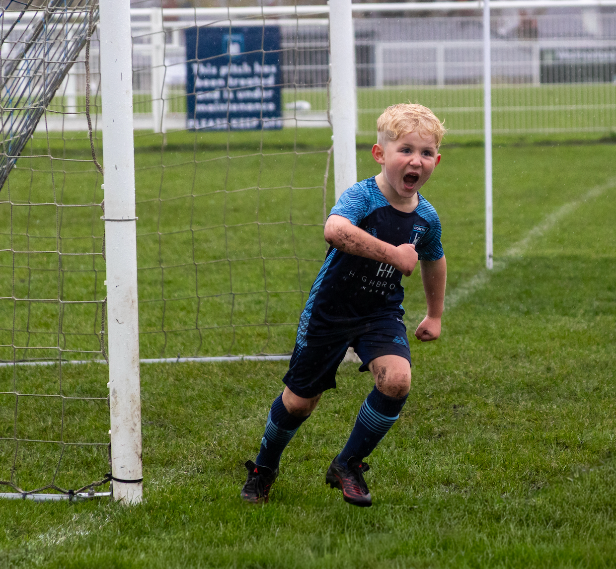 Young soccer players practicing drills near goal posts on grass field.