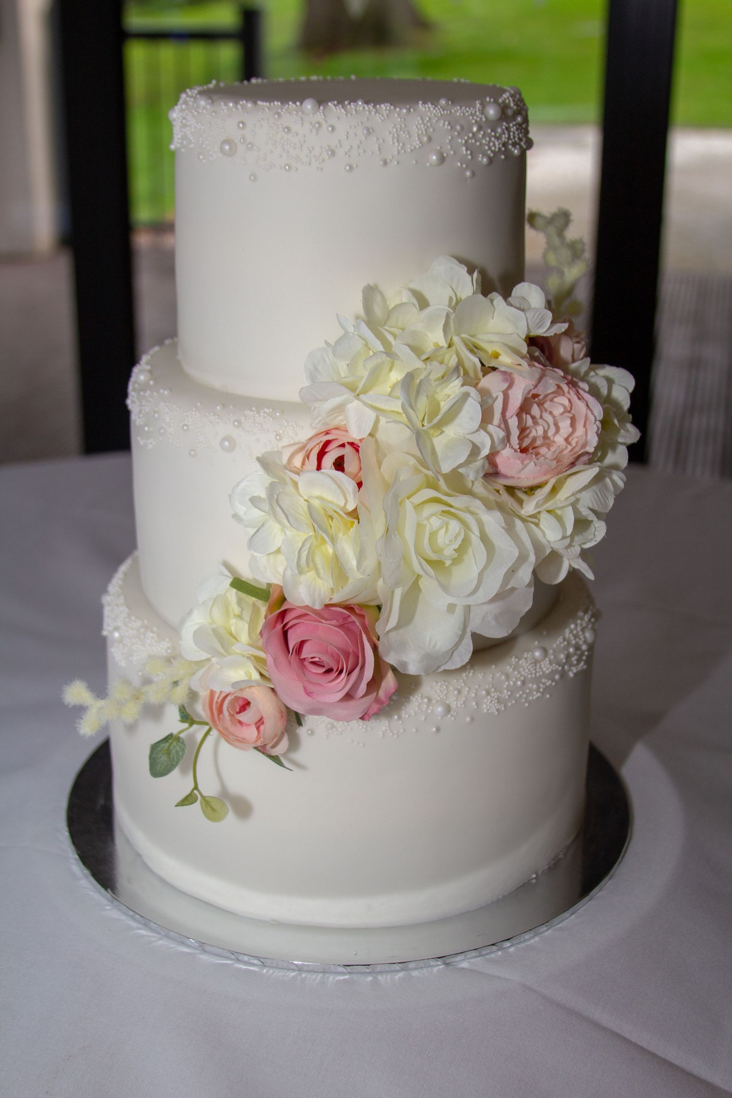 Elegant three-tier white wedding cake decorated with cascading pink and ivory sugar roses.
