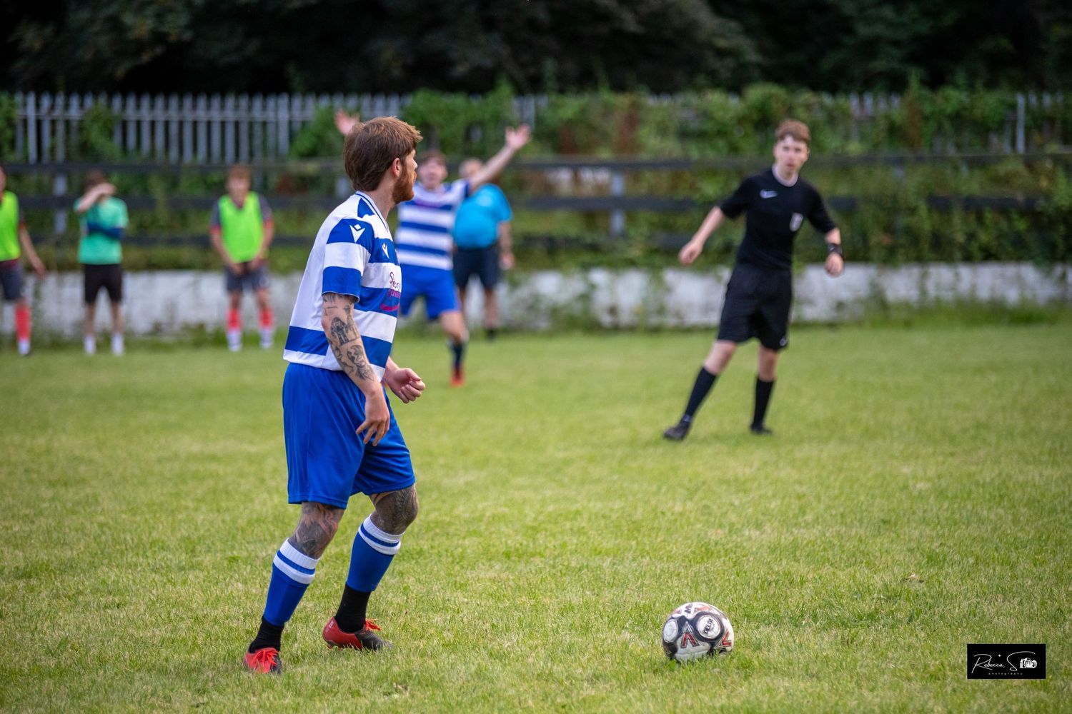 Soccer players in blue and striped uniforms compete for the ball on a grass field during a match.