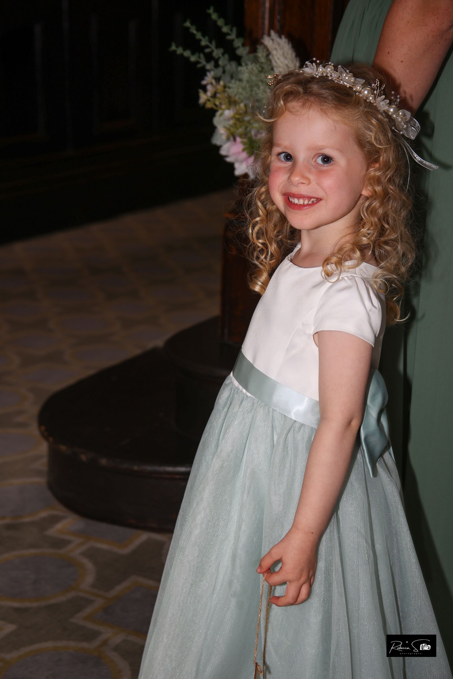A young flower girl in a mint green dress wears a delicate floral crown.