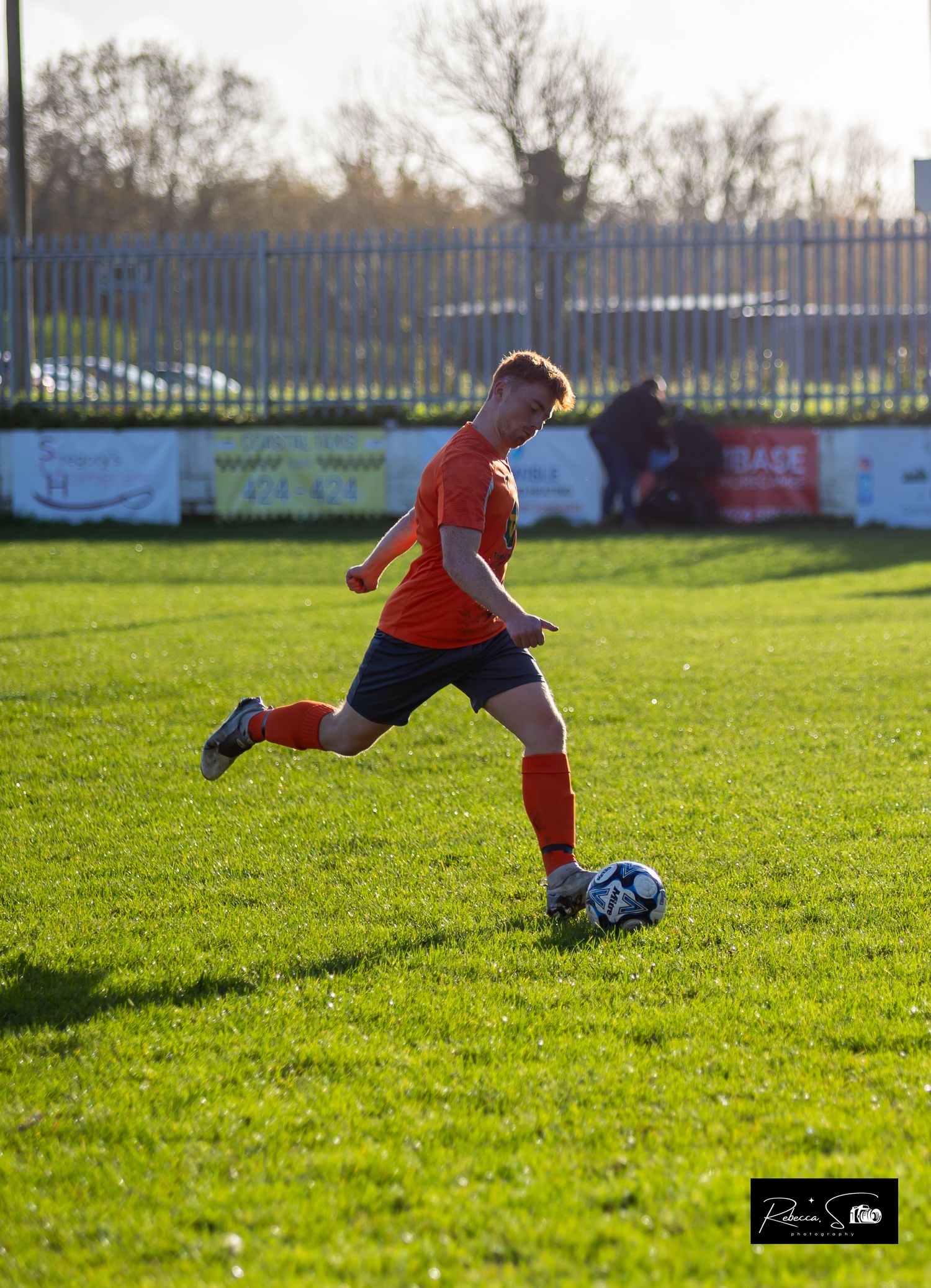 Soccer player in orange jersey dribbling ball on sunny grass field.