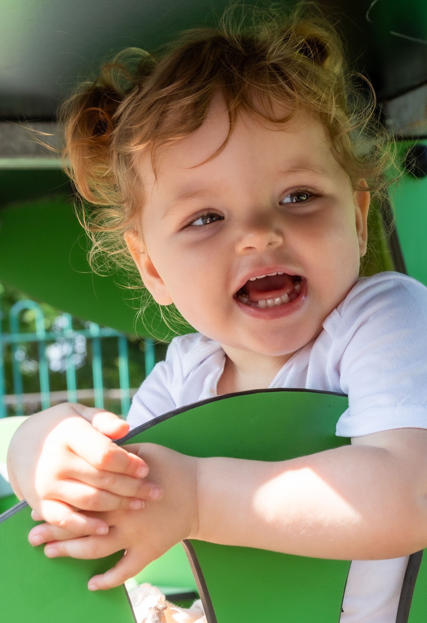 Playful toddler in white t-shirt laughing and playing outdoors.