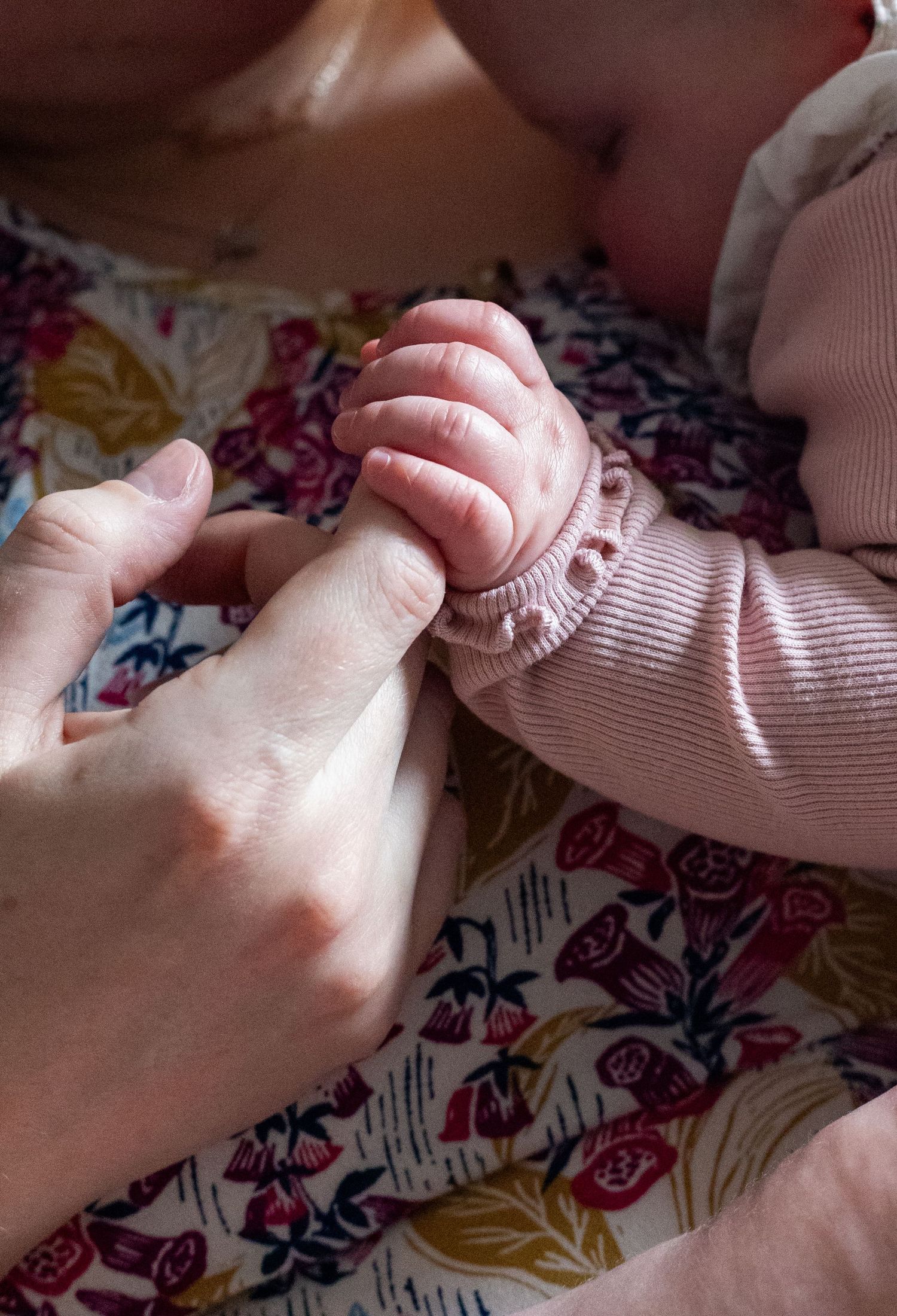 Gentle holding of tiny baby fingers against floral patterned background.