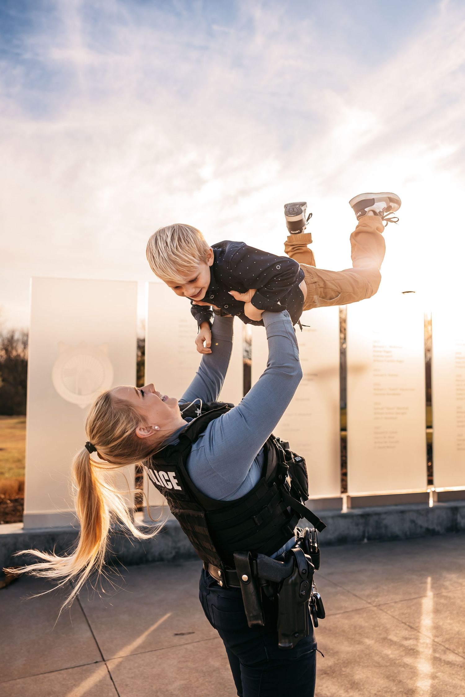 Police officer in uniform playfully lifting a small child against sunset sky.