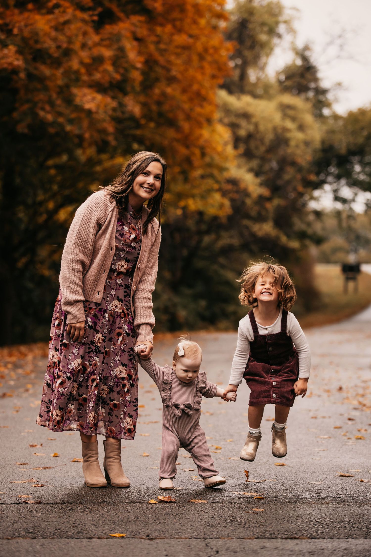A playful autumn photoshoot showing jumping and playing on a leaf-covered path in coordinating brown outfits.