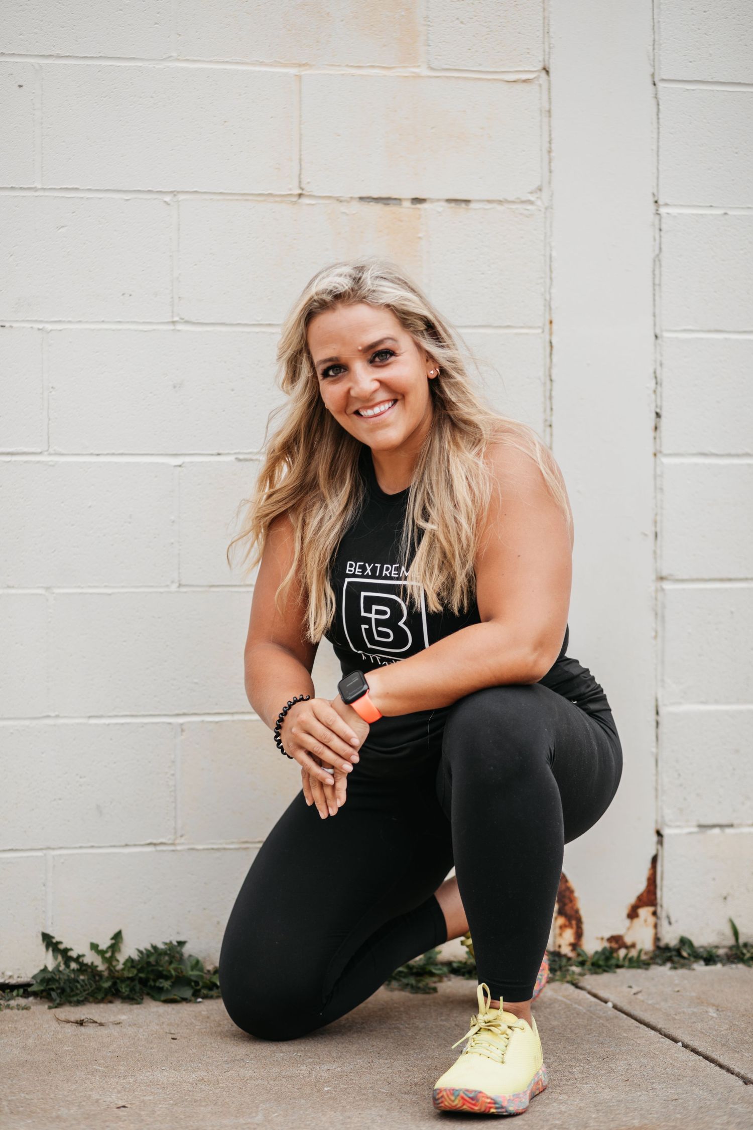 Athletic figure in black workout attire posing against a white brick wall.