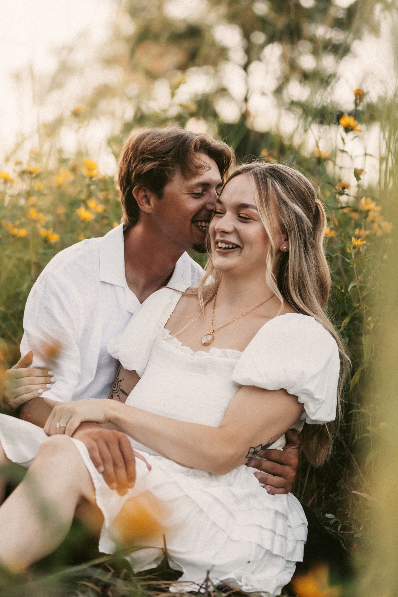 Happy couple sharing laughter while sitting in a blooming wildflower field.