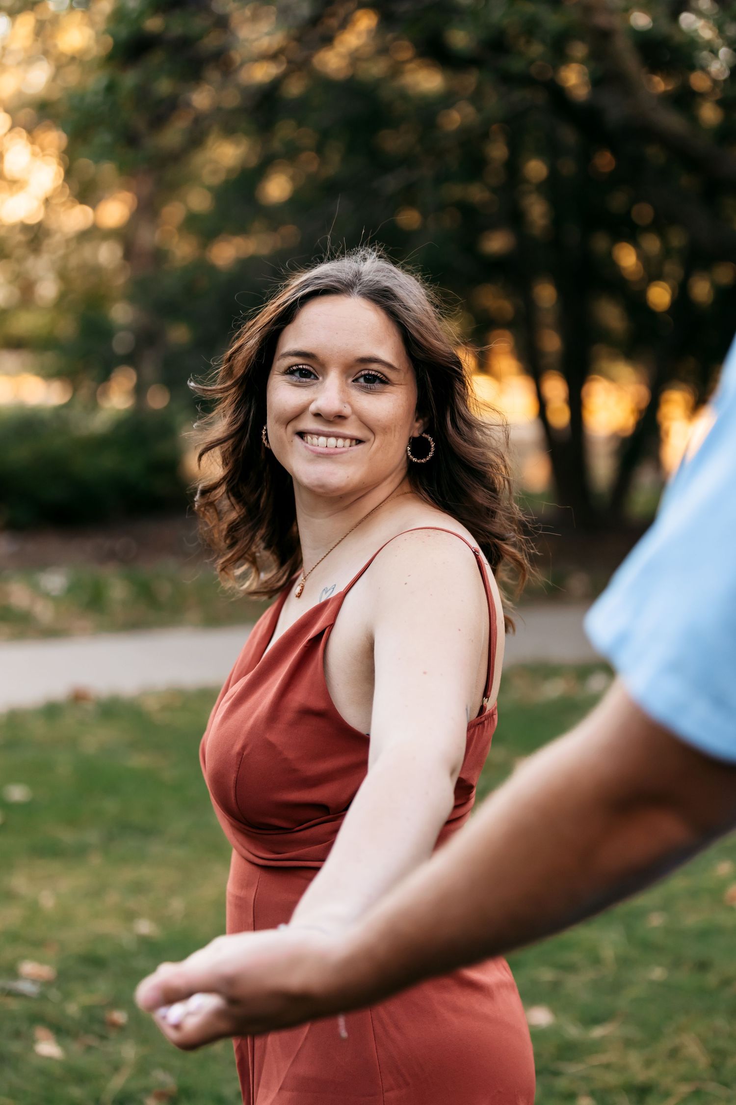 A person in a burgundy top spins joyfully in an outdoor autumn setting during golden hour.
