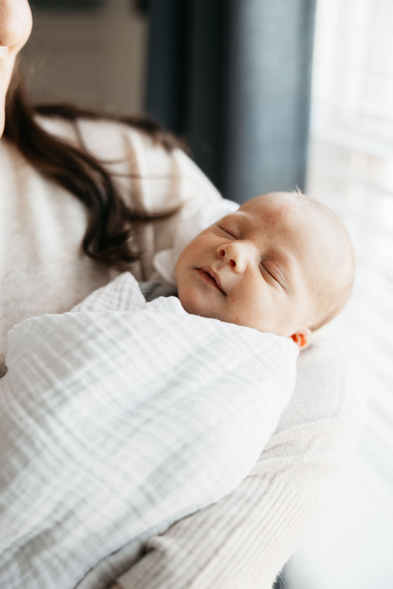 Peaceful sleeping newborn baby wrapped in white swaddle blanket.
