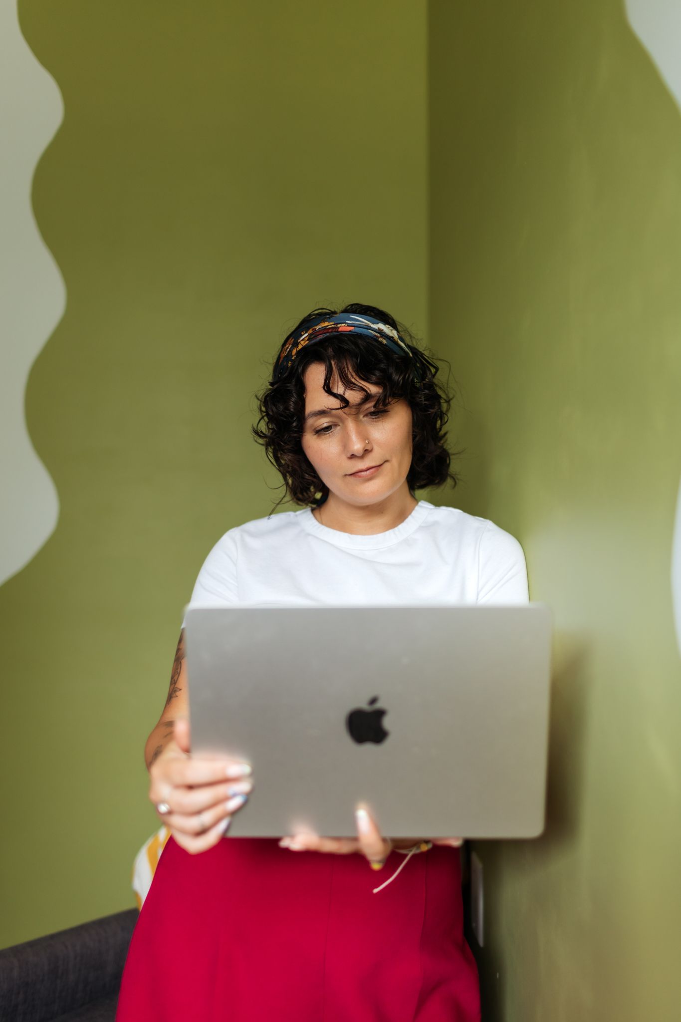 Someone working on a MacBook laptop against a green wall background.