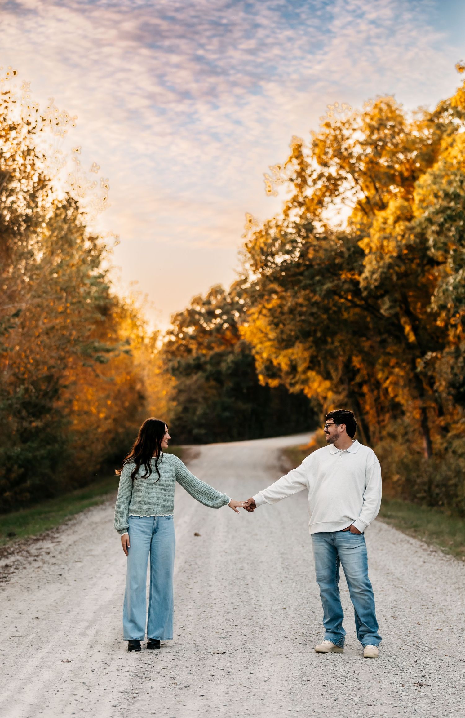 Couple holding hands while walking on a gravel path surrounded by golden autumn trees.