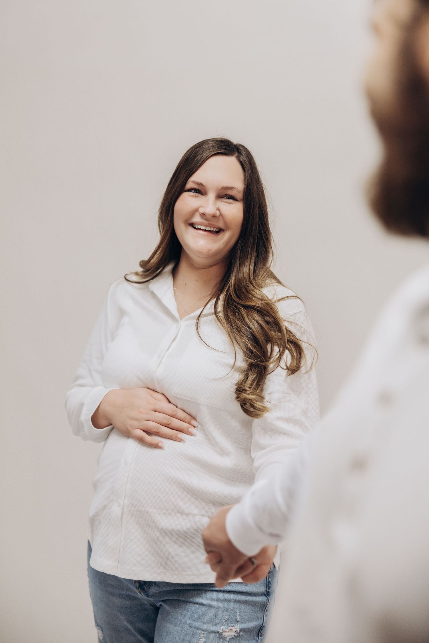 Person in white button-down shirt and jeans laughs joyfully during casual photo session.