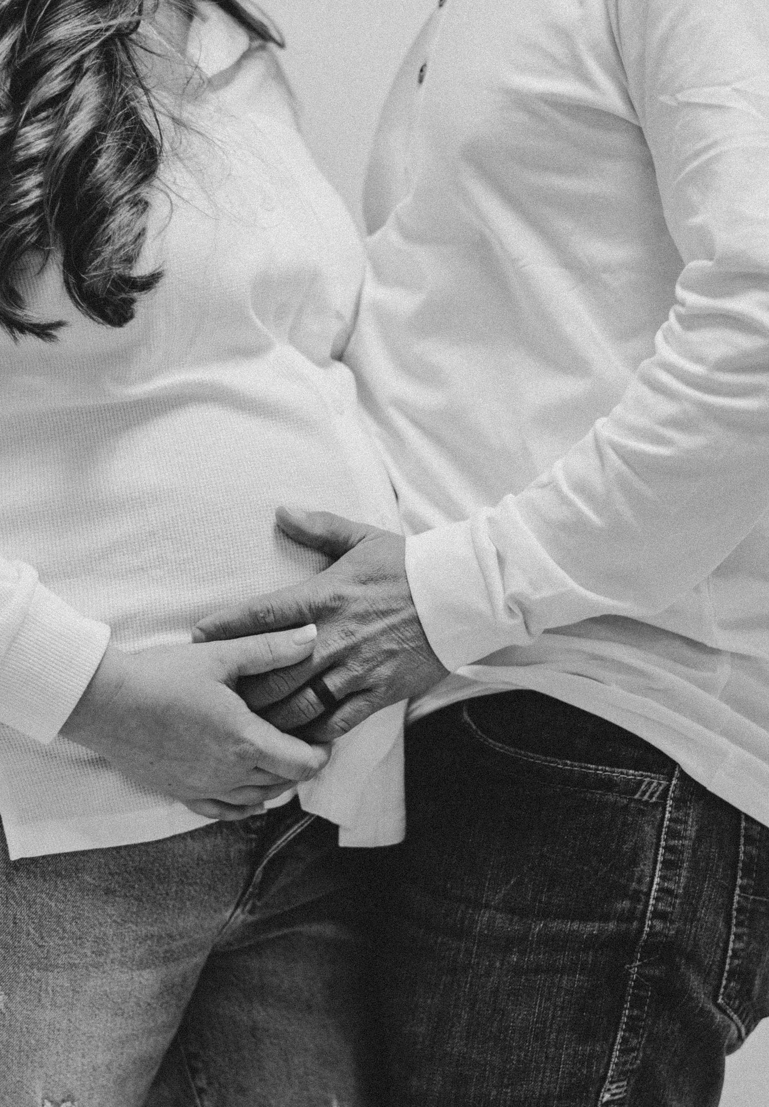 Black and white intimate maternity photo showing hands on pregnant belly.