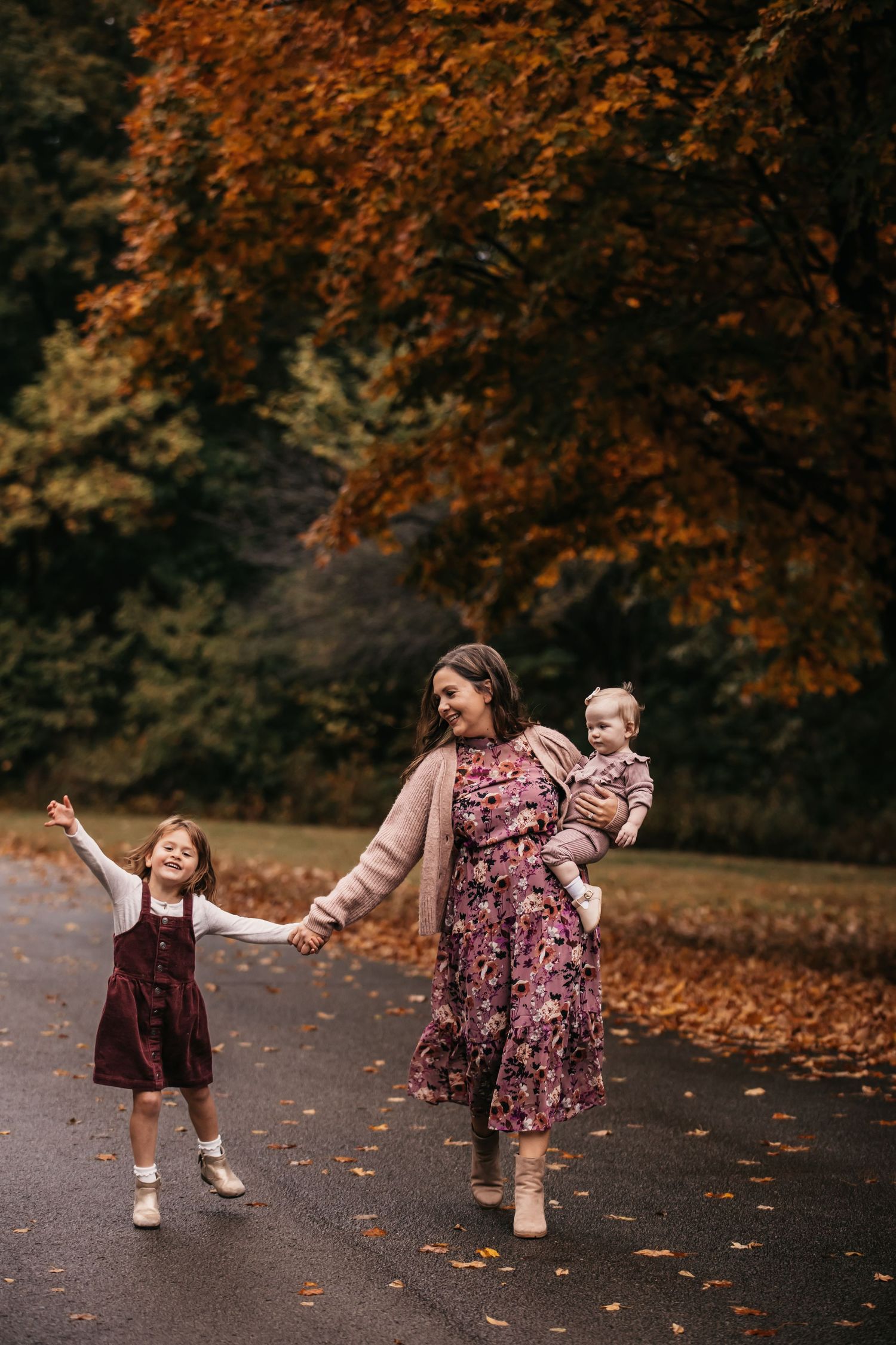 Children twirling and dancing in burgundy dresses among fallen autumn leaves.