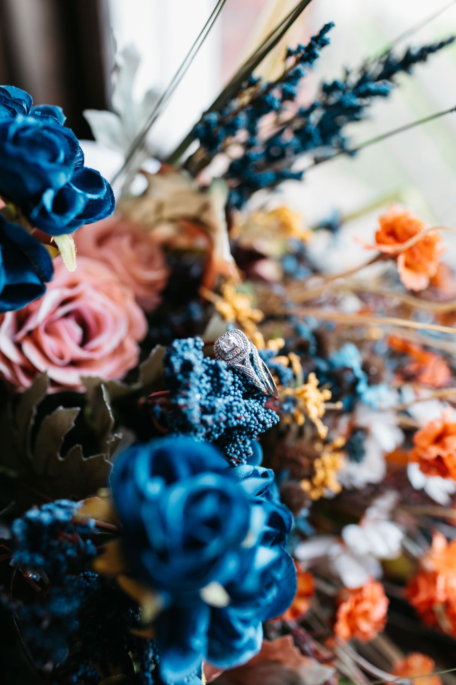 Wedding floral arrangement featuring vibrant blue and coral roses with delicate details.