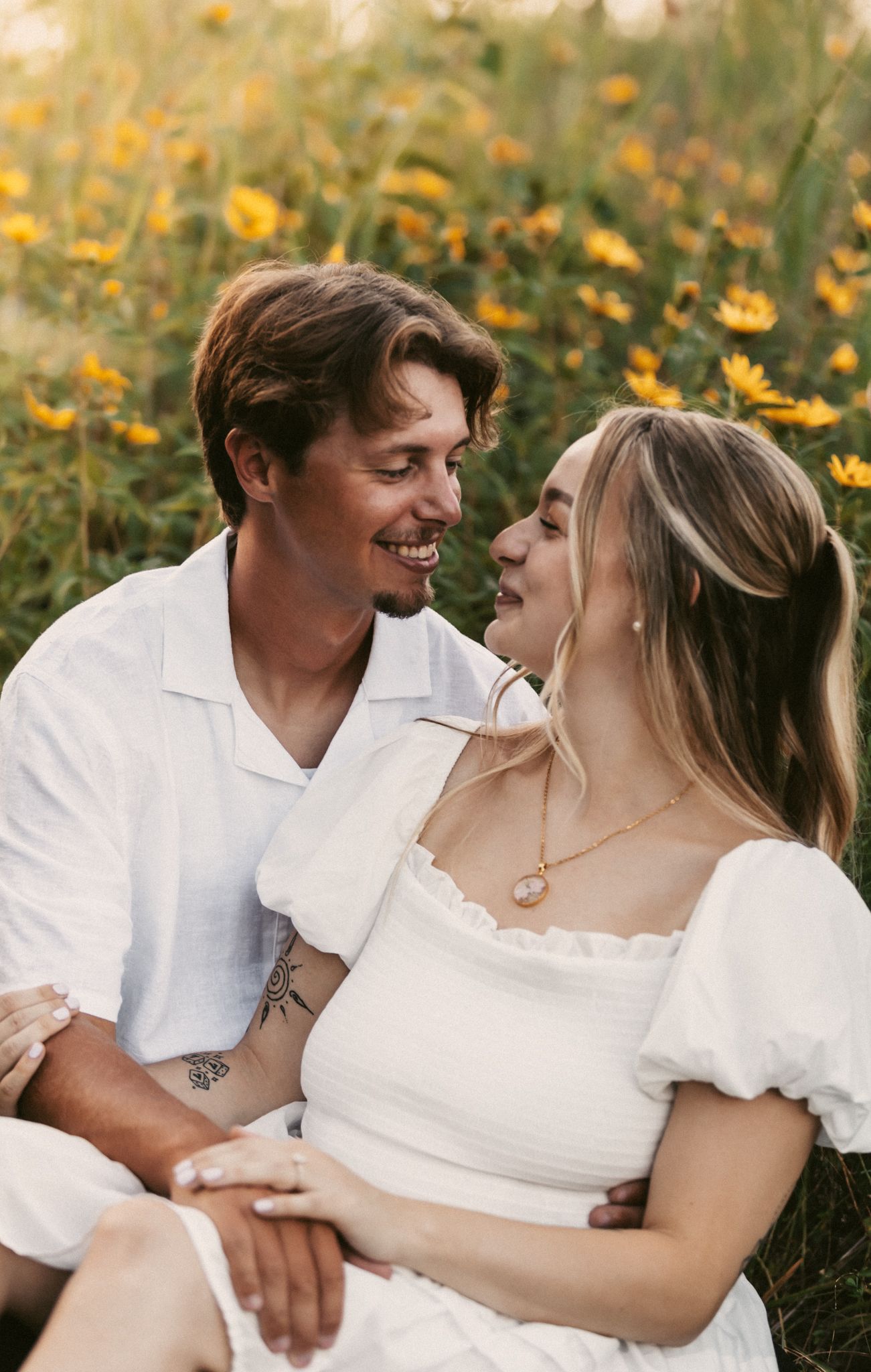 Joyful couple laughing together in a field of yellow wildflowers at sunset.