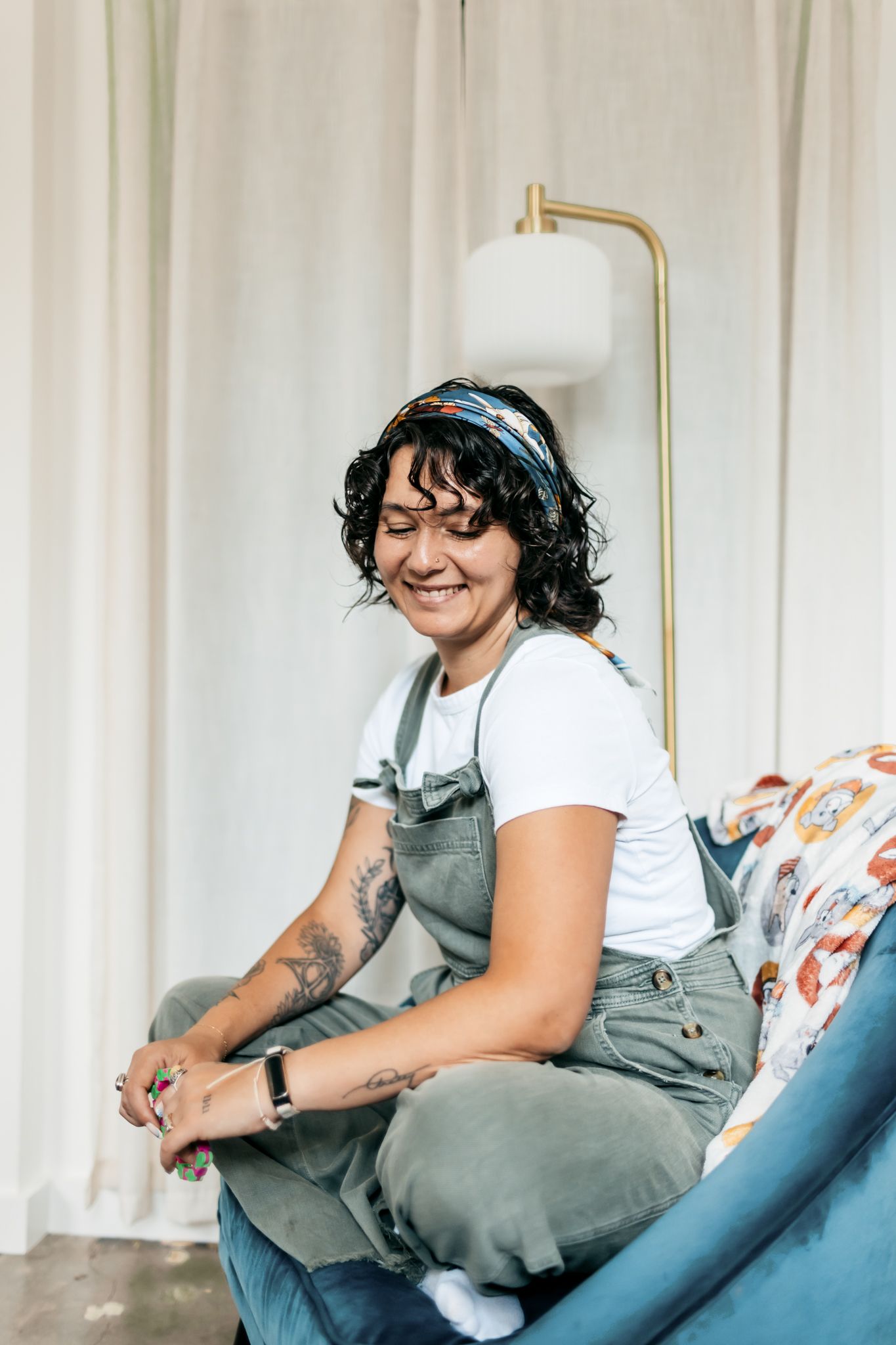 Casual indoor portrait on a blue couch wearing gray overalls and a white t-shirt.