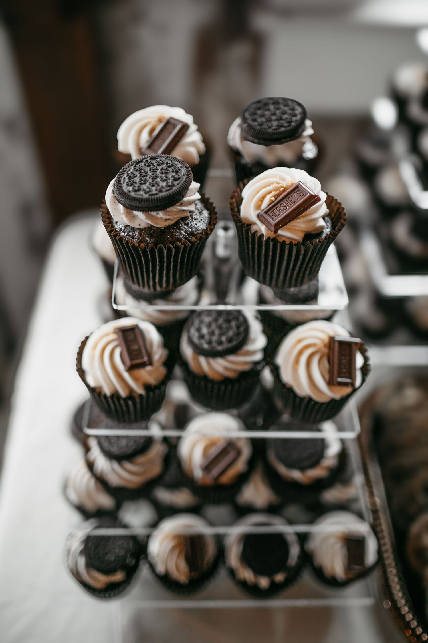 Chocolate cupcakes decorated with Oreos and swirled frosting displayed on clear stands.