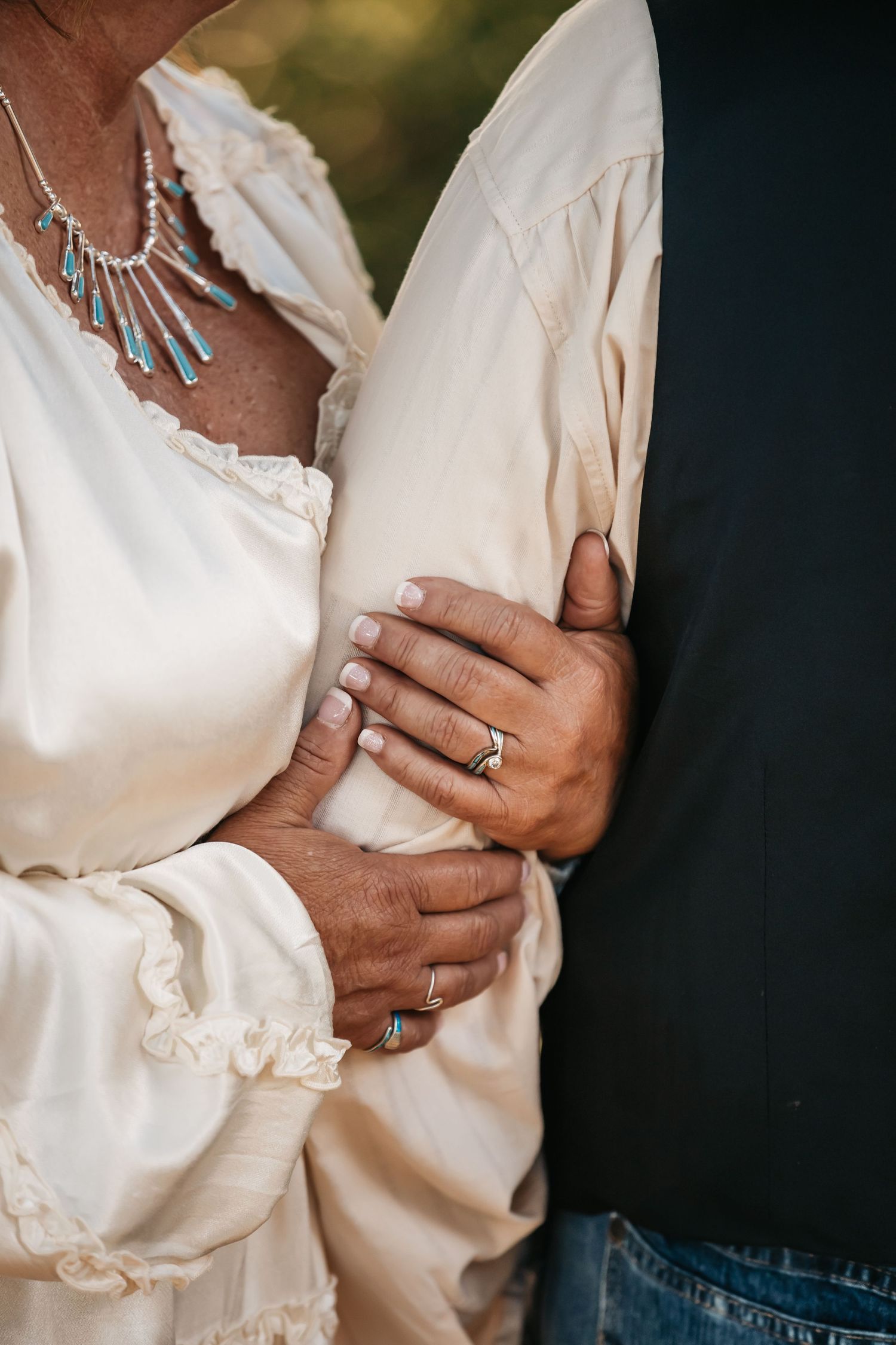 Close-up of hands embracing showing wedding rings and white lace sleeves.