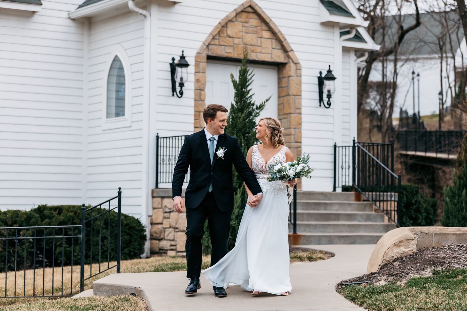 Wedding couple walking outside white chapel with elegant architecture.