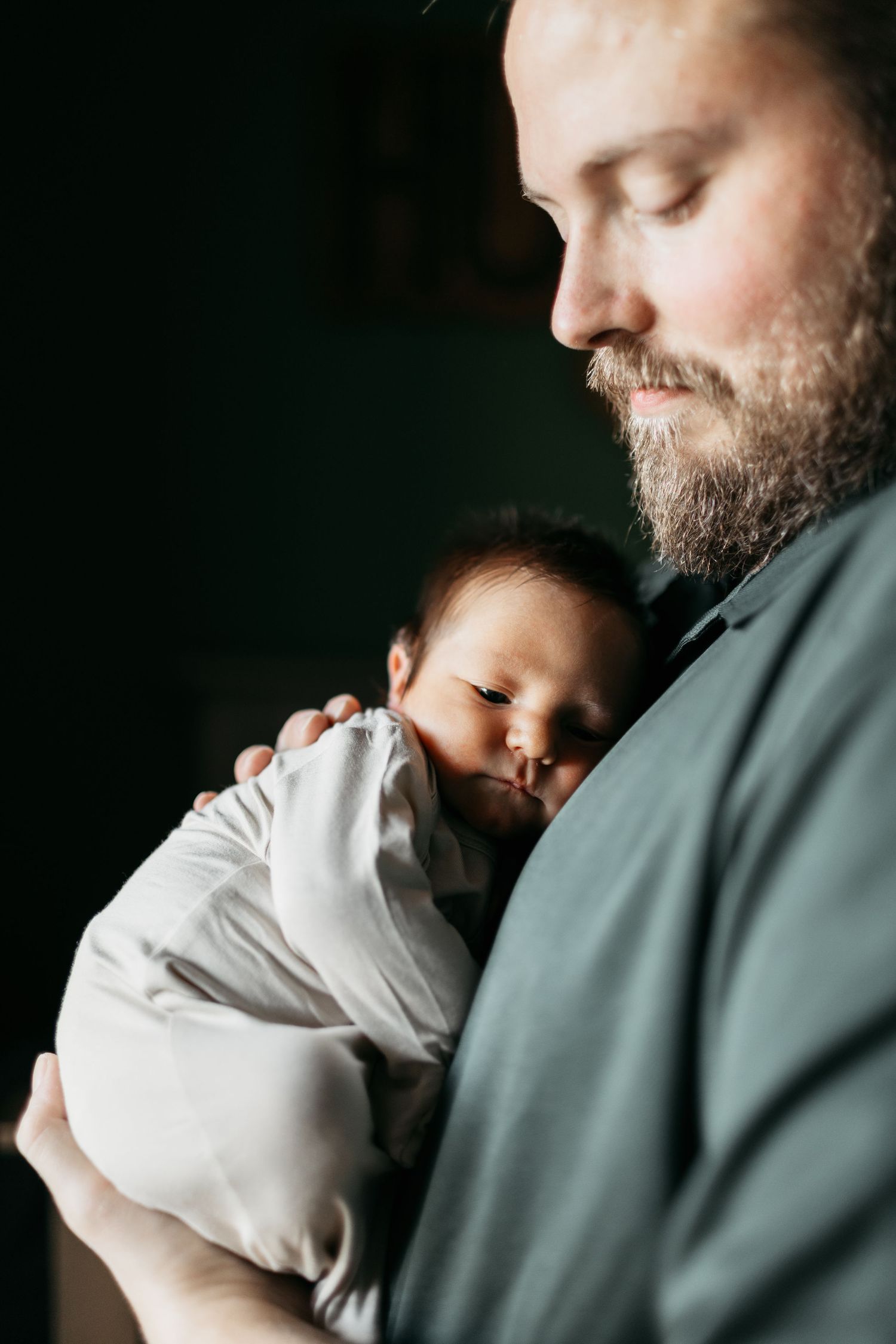 Tender moment between father and sleeping newborn baby in dramatic lighting.
