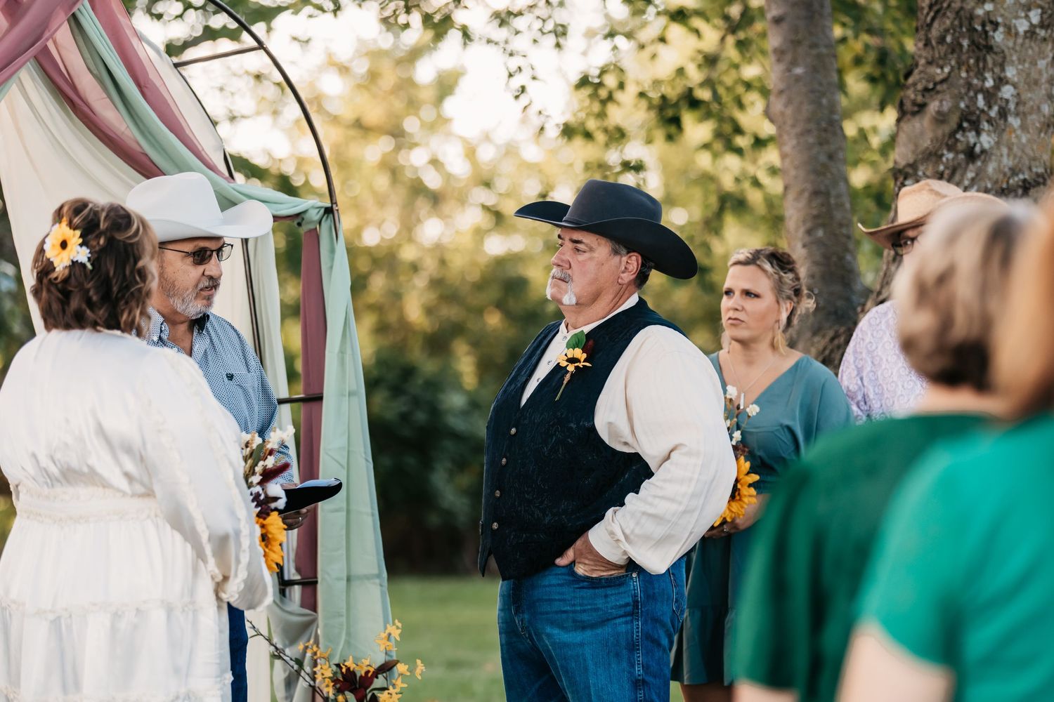 Outdoor wedding ceremony guests gathered under trees at sunset.