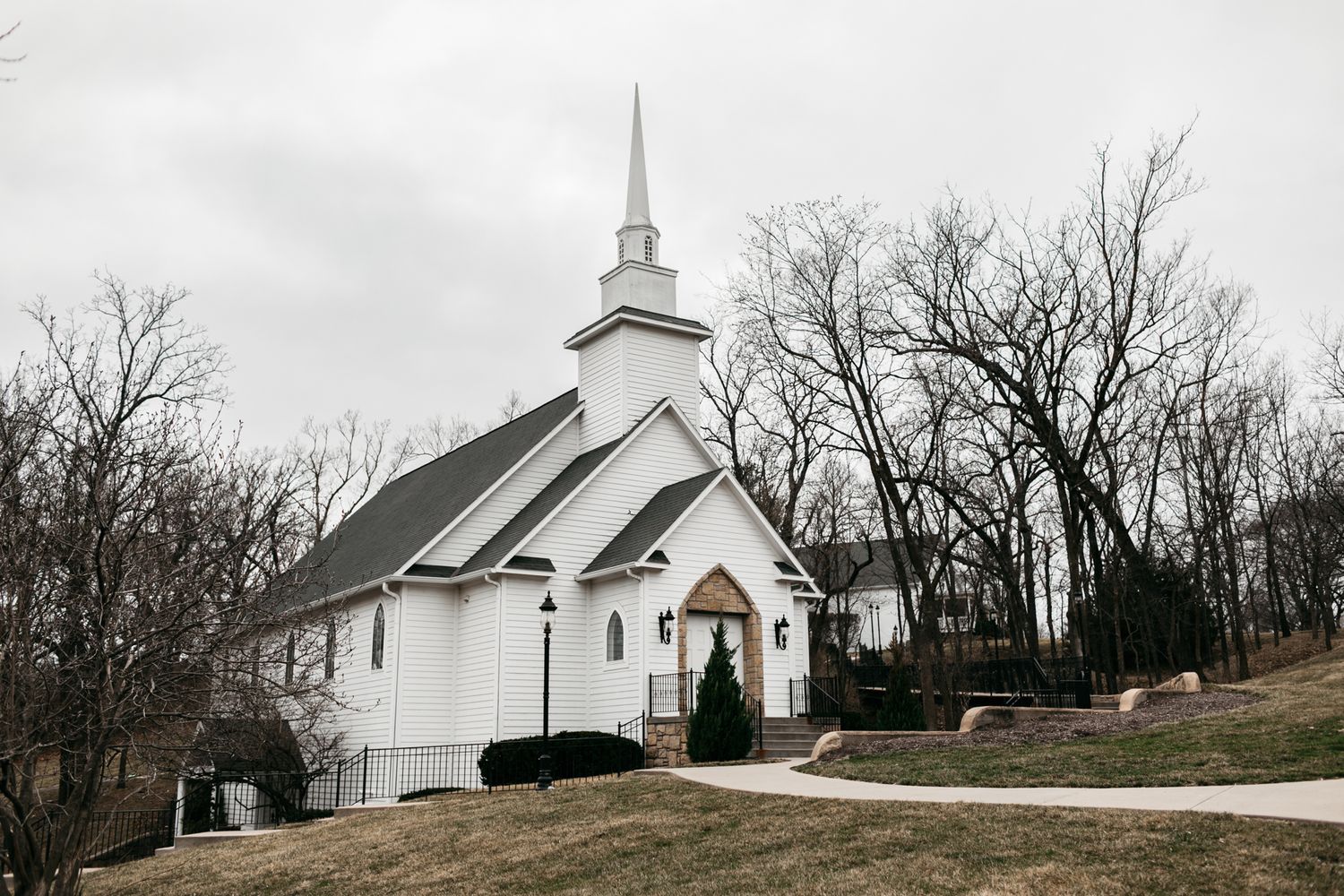 Panoramic view of a white country church with steeple against bare winter trees.