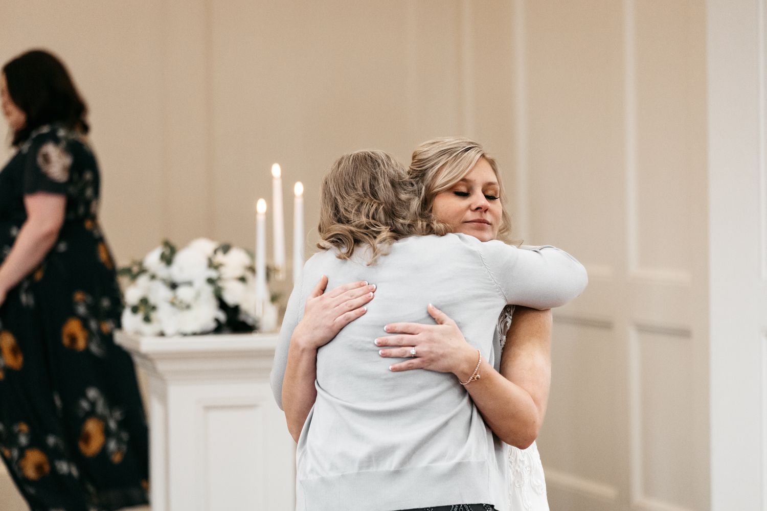 Wedding party members sharing emotional hugs and embraces in a bright indoor space.