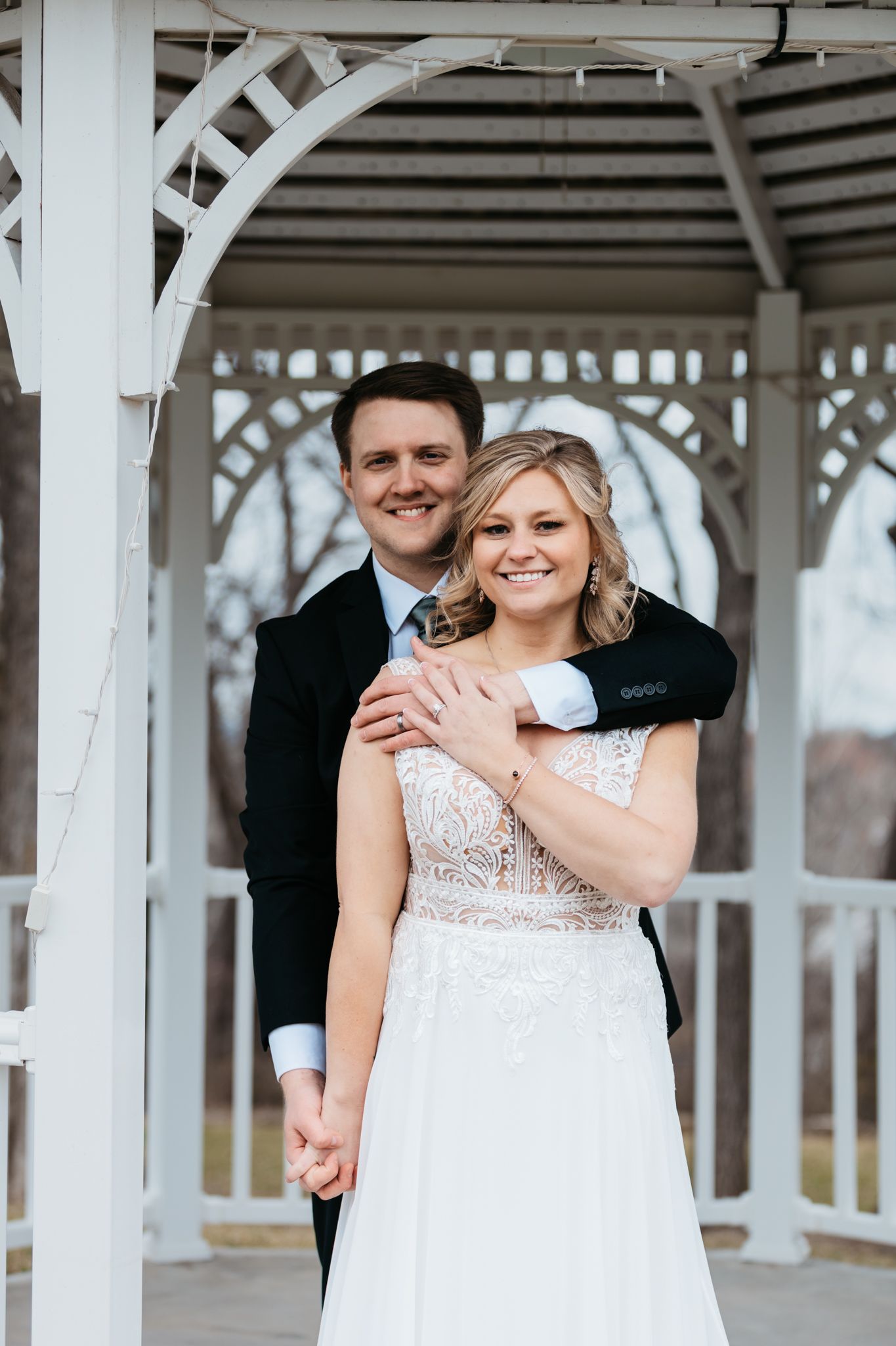 Couple sharing joyful moments under white gazebo during wedding celebration.