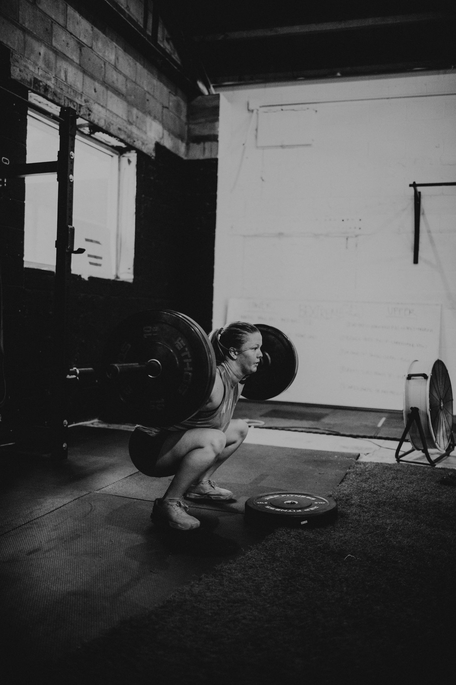 Black and white sequence of an athlete performing barbell snatch movements in a dark gym.