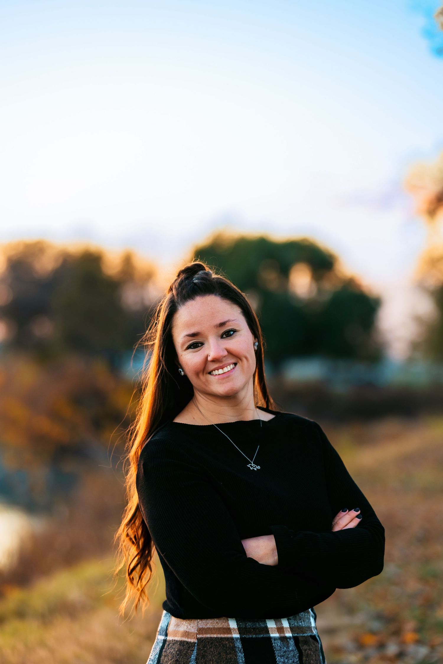Outdoor portrait at sunset wearing a black sweater and plaid skirt with arms crossed.