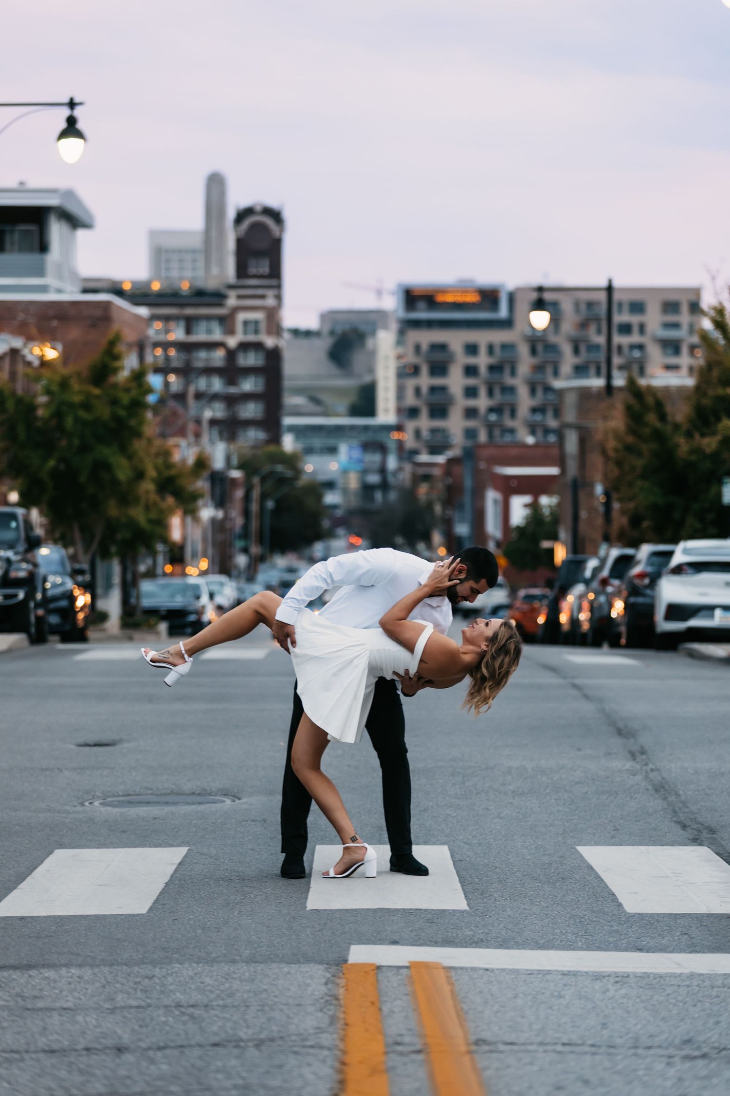 Urban couple photography with dramatic dips and poses on a city crosswalk at twilight.
