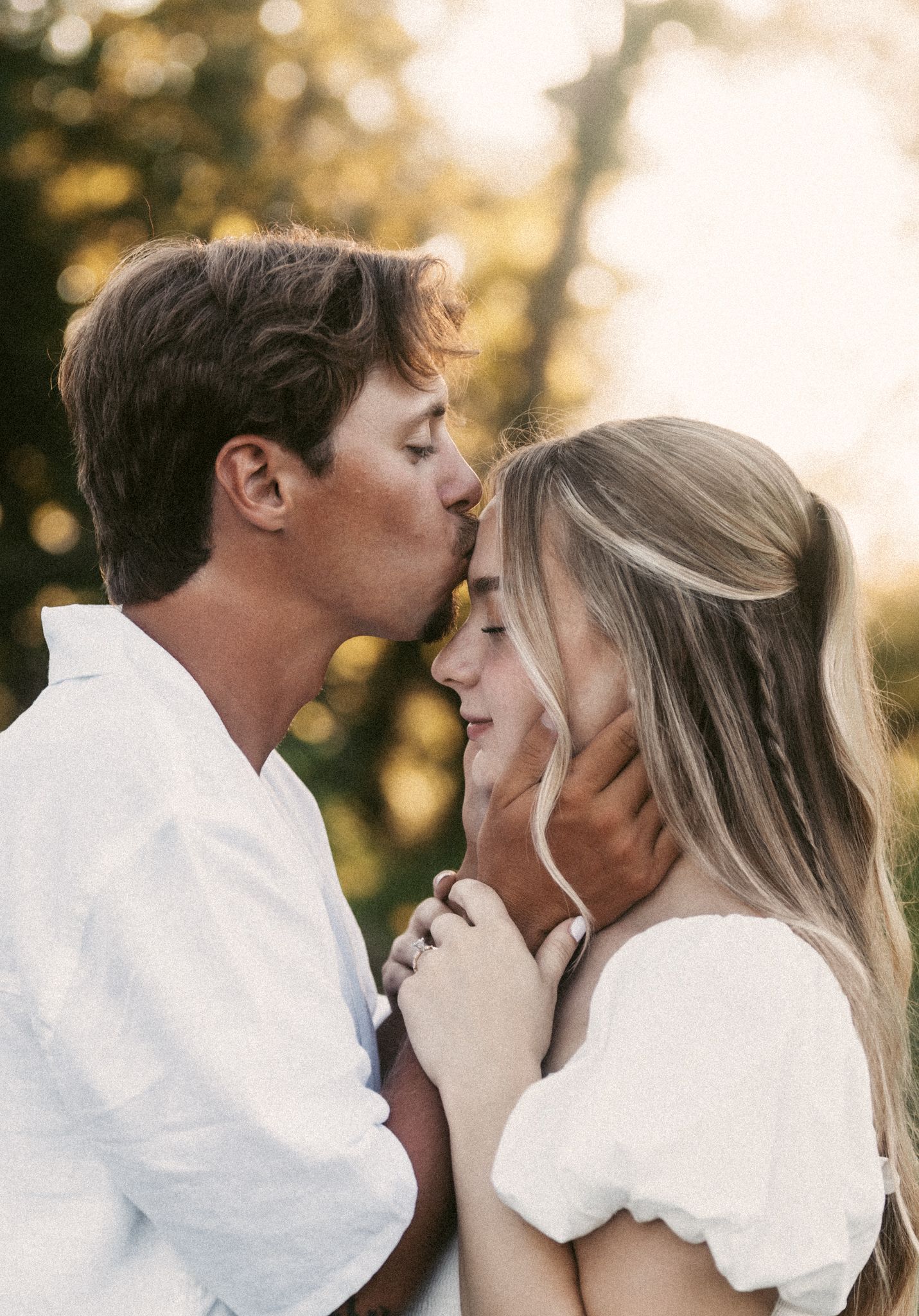 Intimate moment captured between couple in white attire during golden hour.