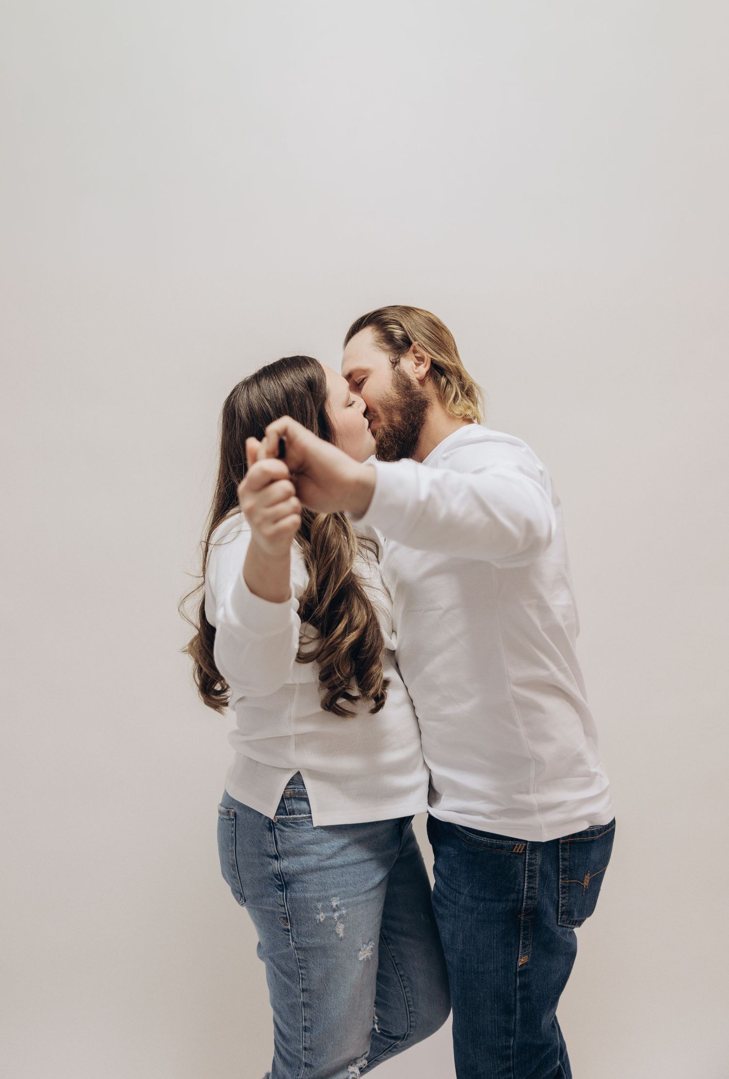 Romantic couple in white shirts and denim embrace in sequence of candid studio shots.