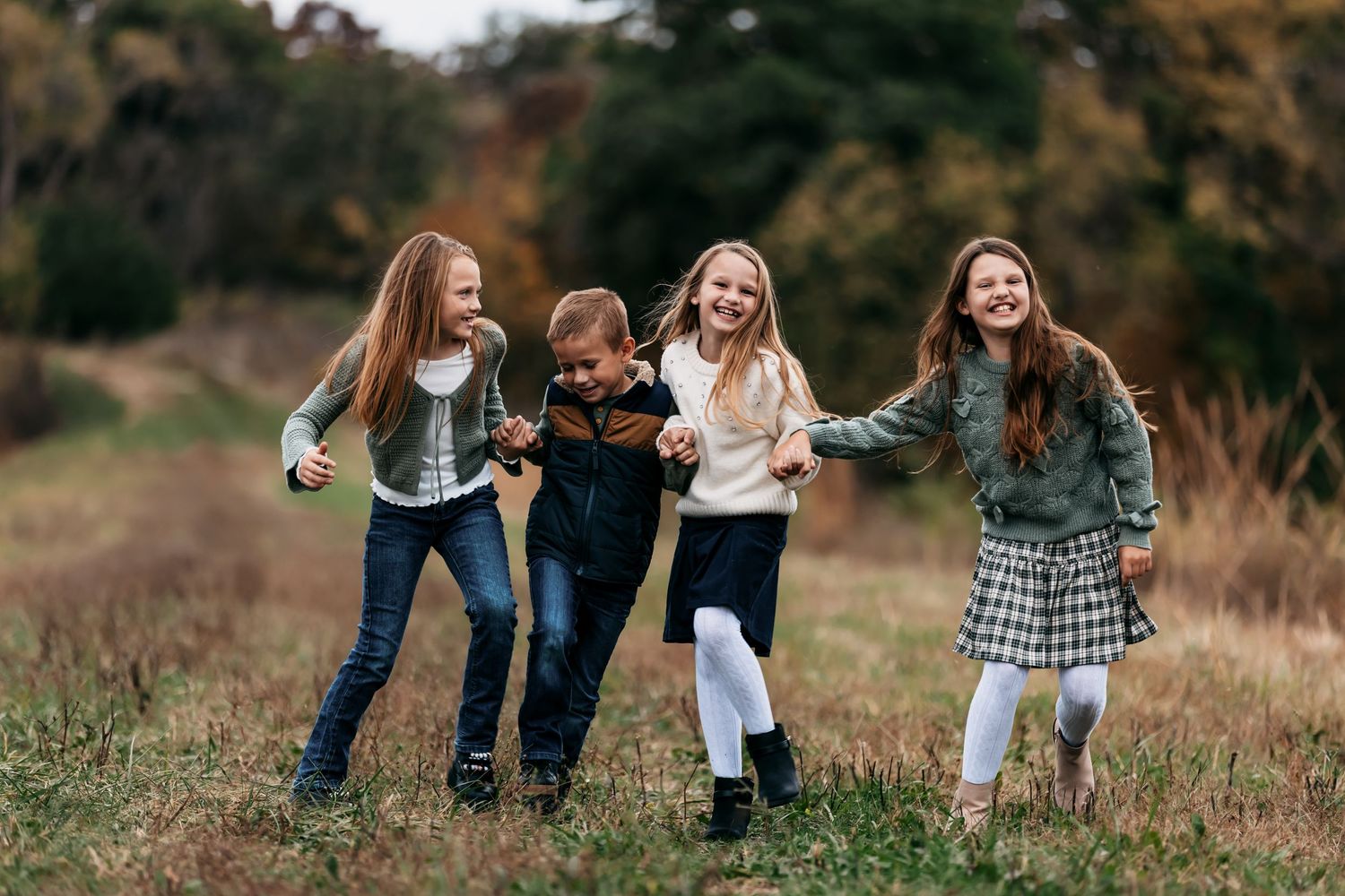 Four friends laughing together while walking through a grassy field during autumn.